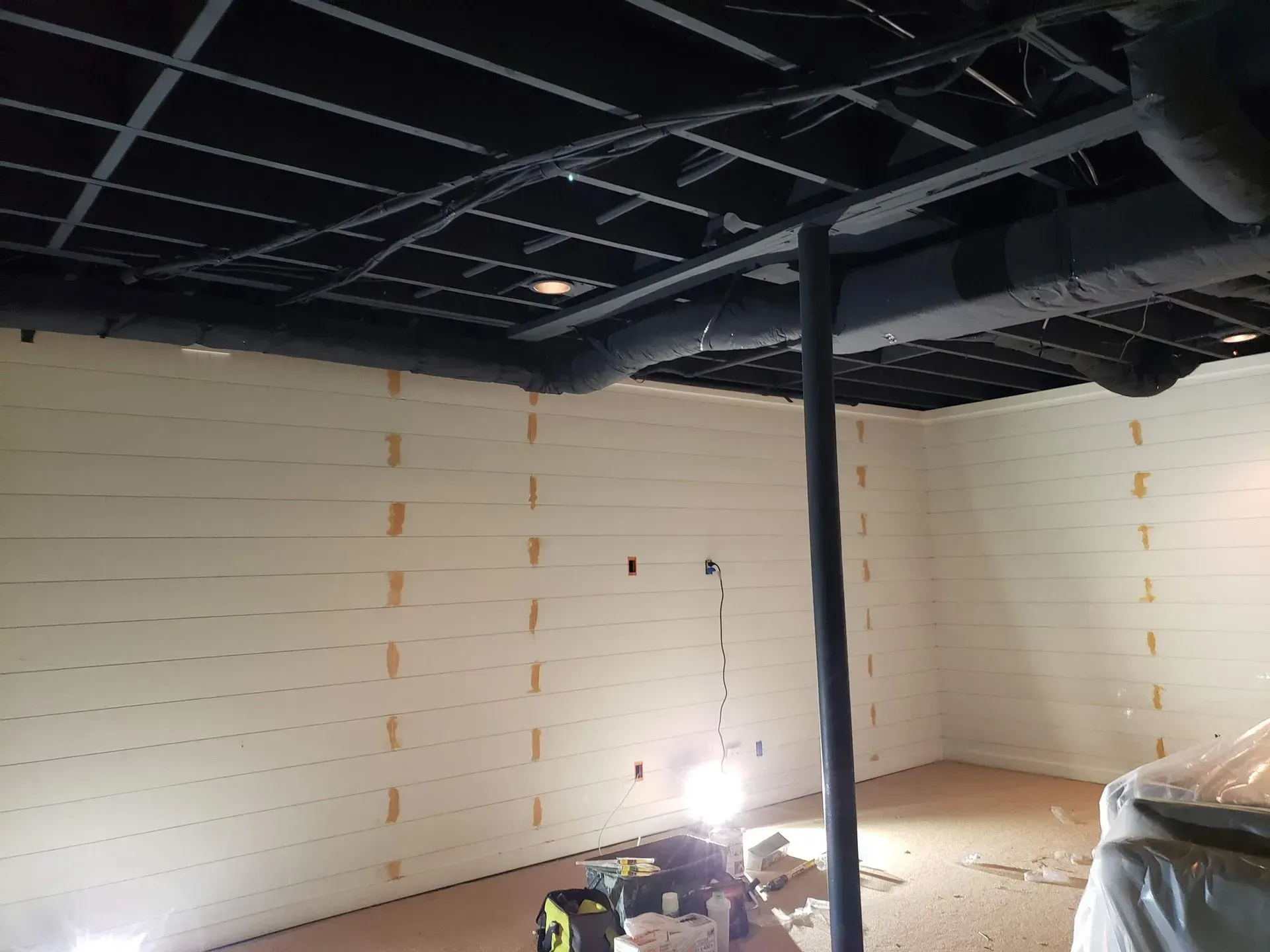 Basement renovation with white planked walls, black ceiling and exposed beams.