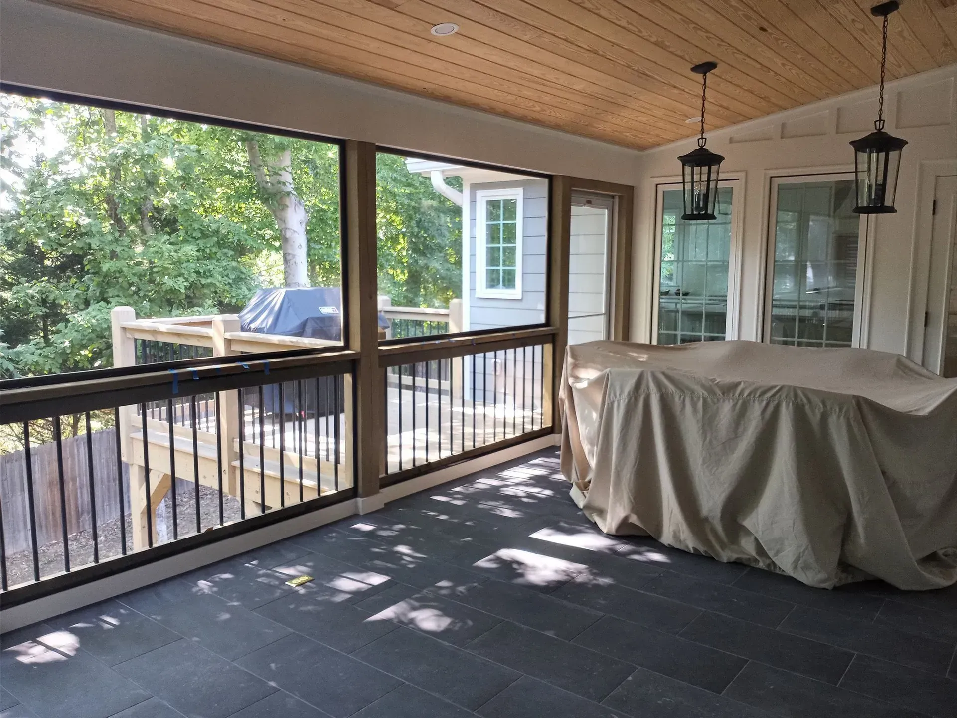 Covered outdoor dining area with dark floor, screen walls, and hanging lanterns.