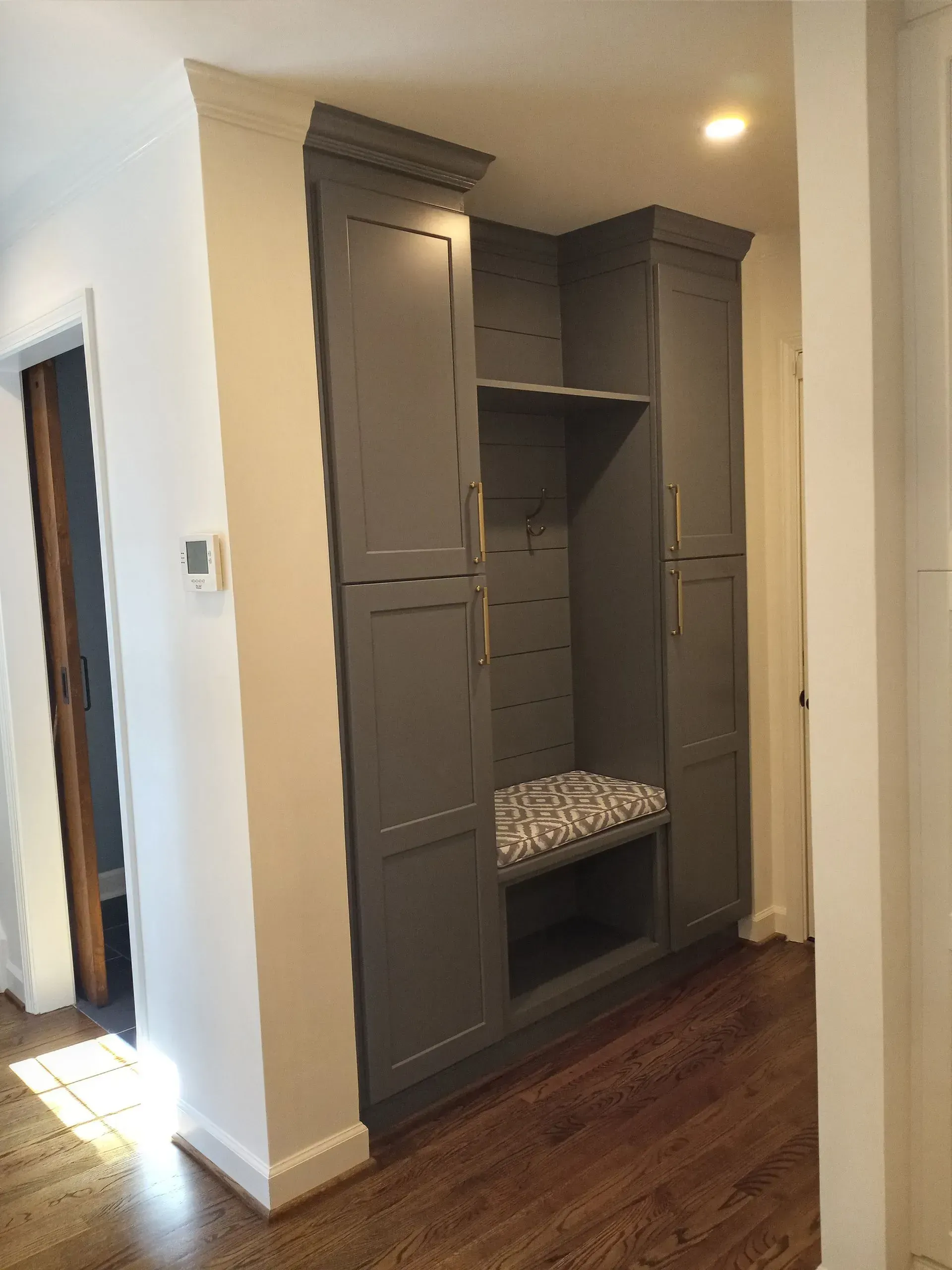 Gray built-in entryway storage unit with bench, shelves, and cabinets. Wooden floors and white walls.