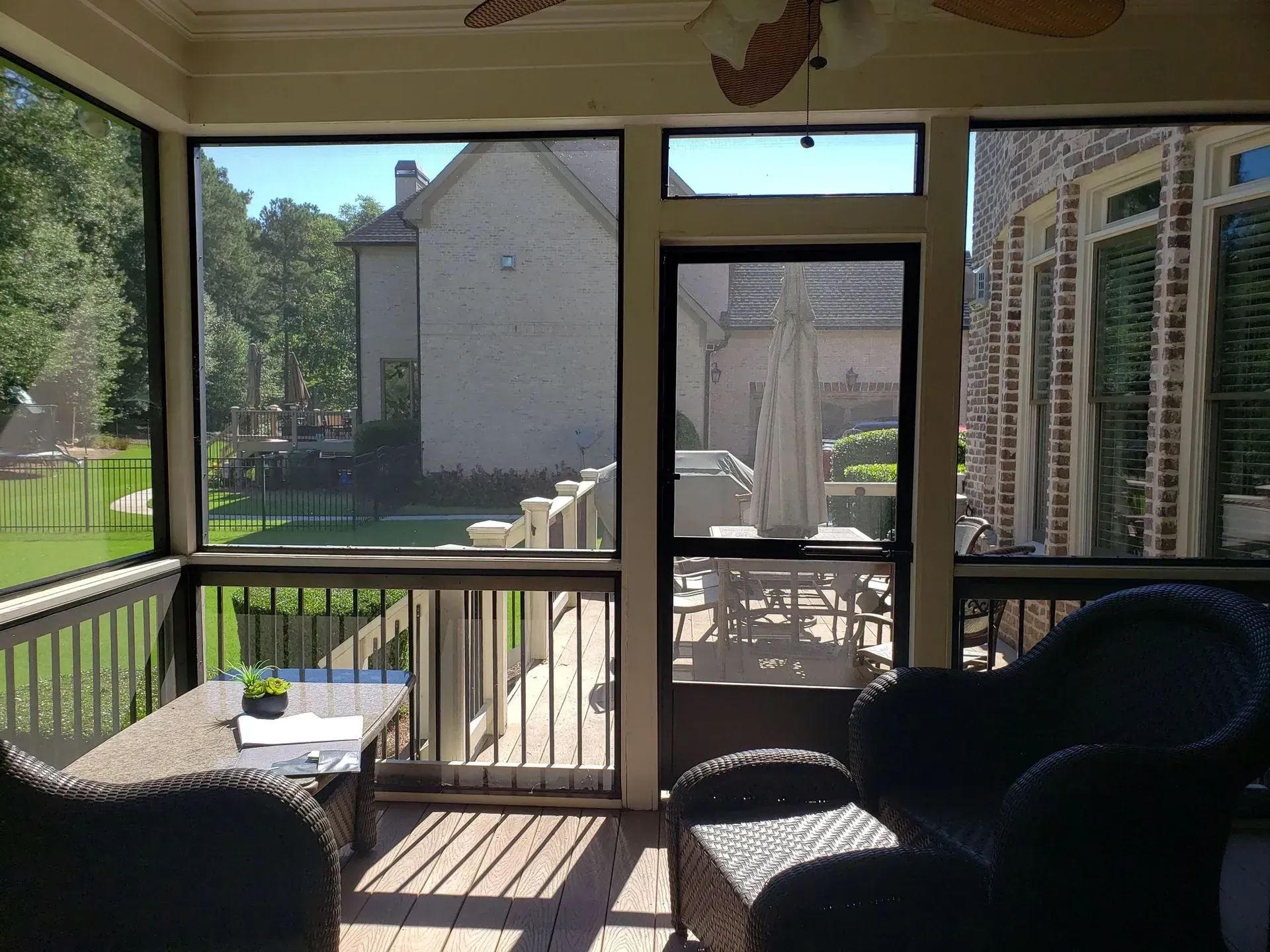 Screened-in porch with wicker furniture and view of a backyard with a house, lake, and trees.