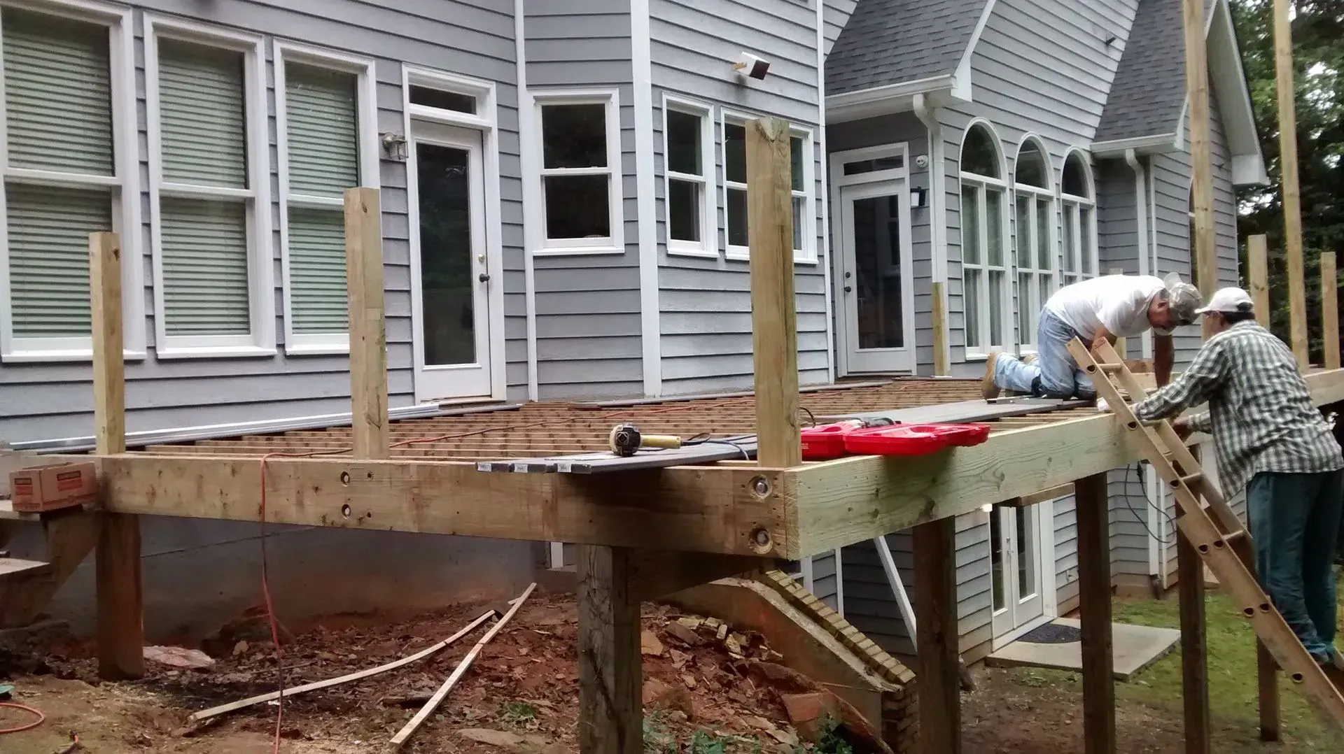 Two people building a wooden deck next to a gray house.