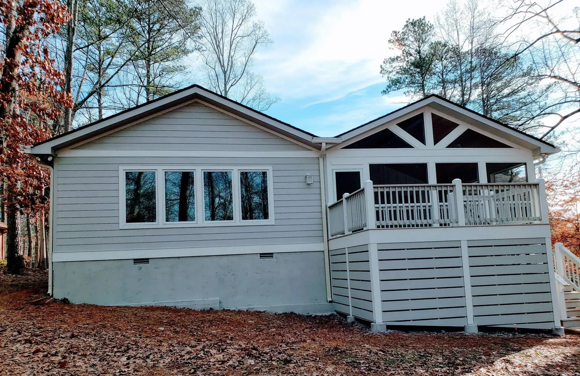 Light blue house with porch and deck, set in a wooded area under a blue sky.