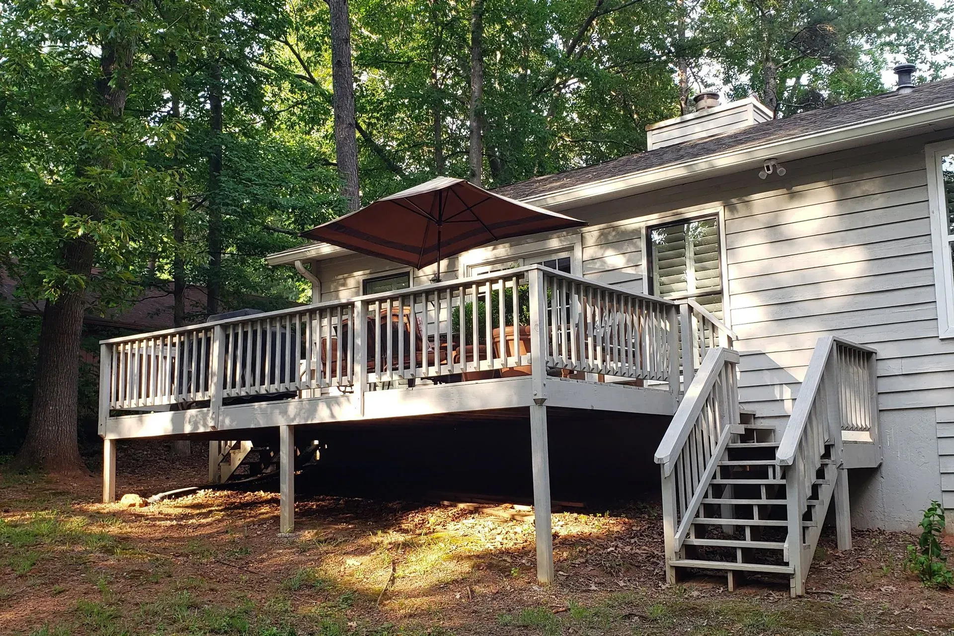 Wooden deck with umbrella, railings, and stairs attached to a house with trees in the background.