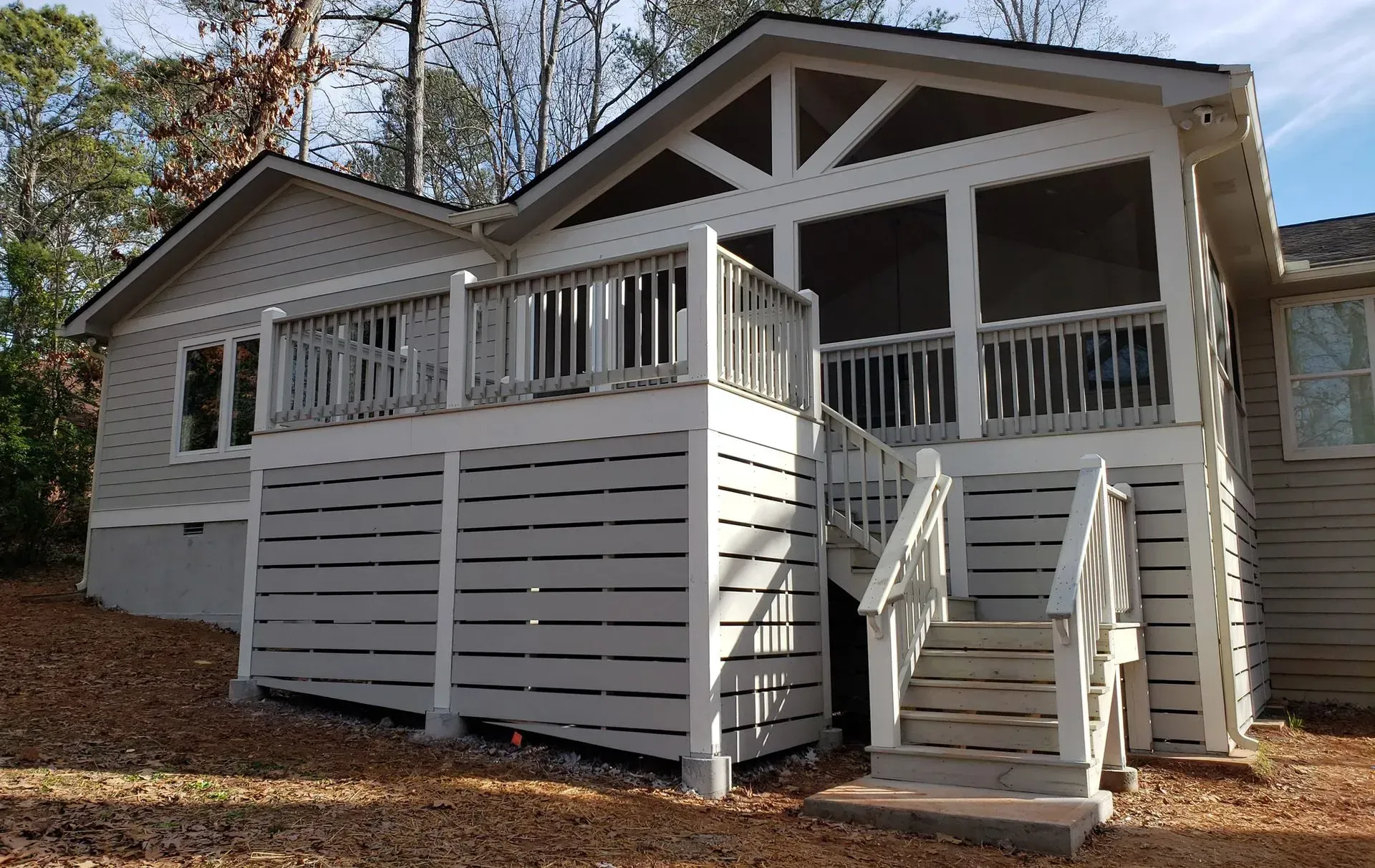 Gray house with a deck and screened porch. White railings and stairs. Trees in the background.