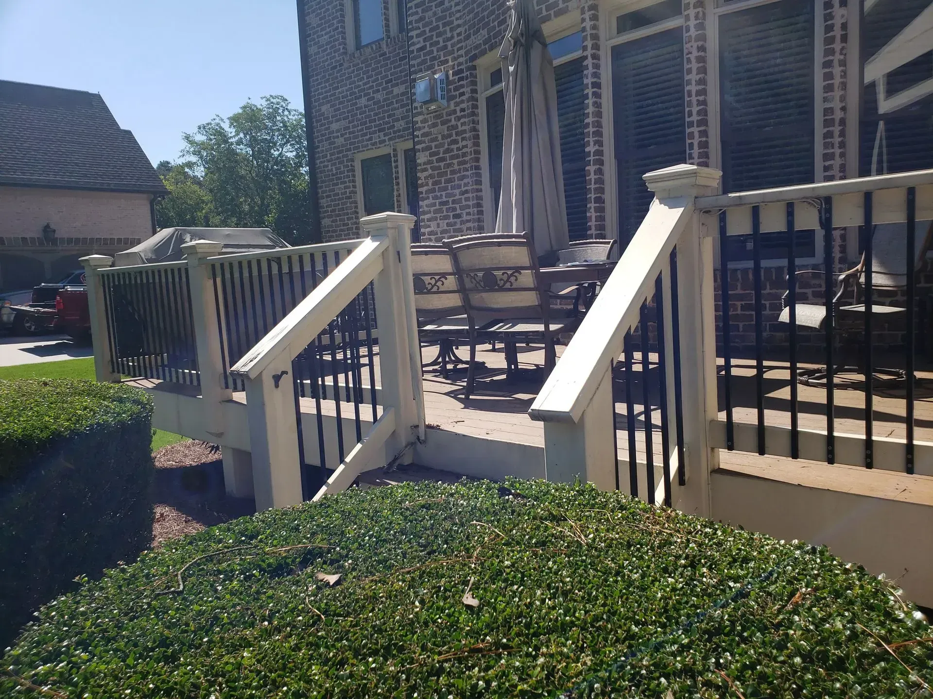 Deck with white railings and black spindles, leading to patio with umbrella and furniture.
