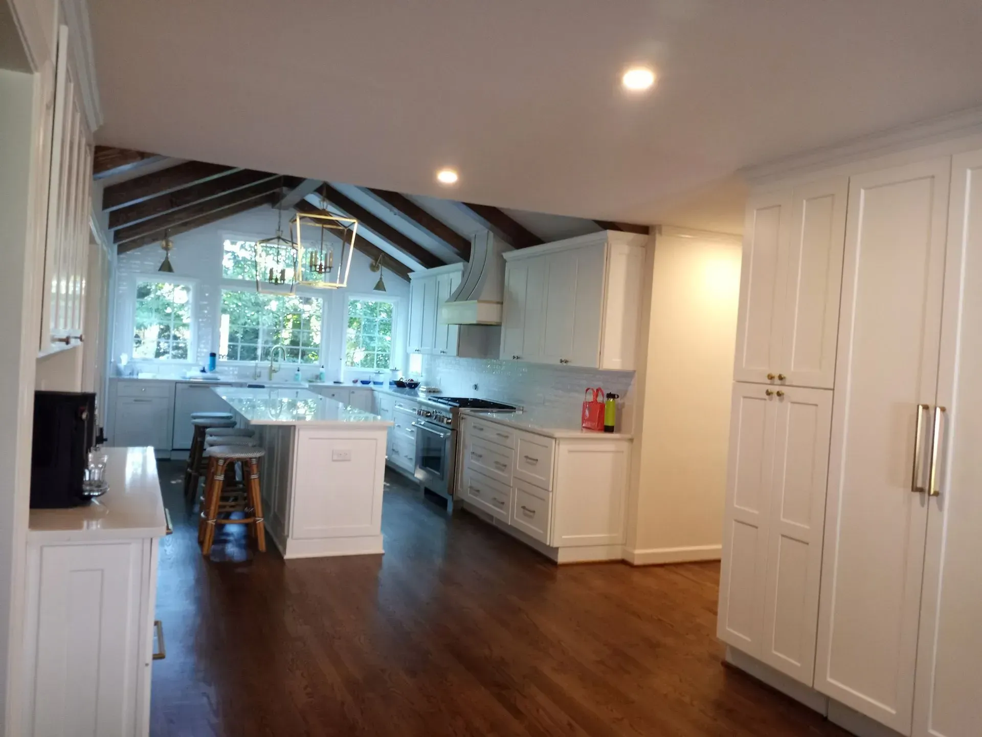 Spacious white kitchen with dark wood floors, white cabinets, and island; a vaulted ceiling with exposed beams.