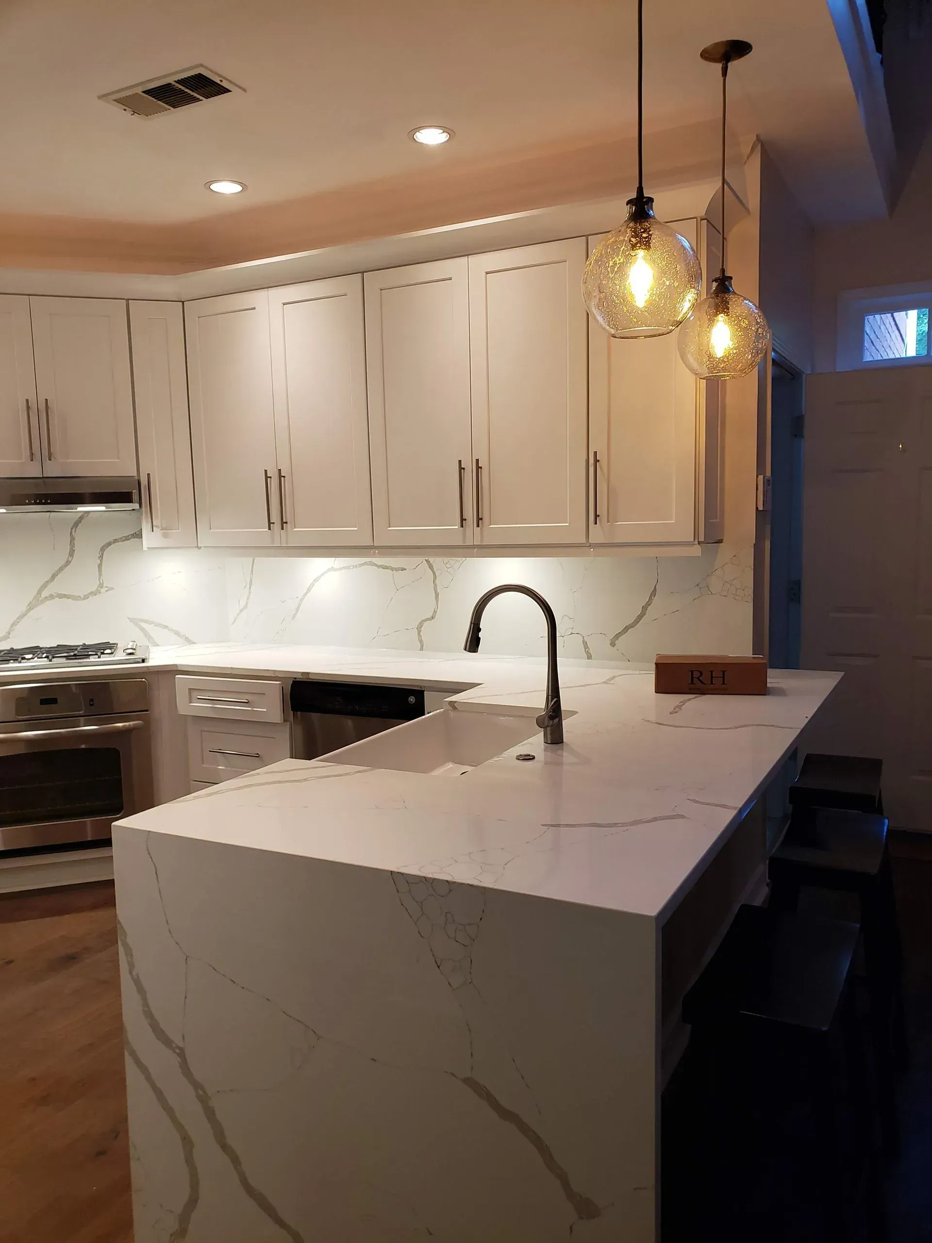 Modern white kitchen with quartz countertops and pendant lights over the island.