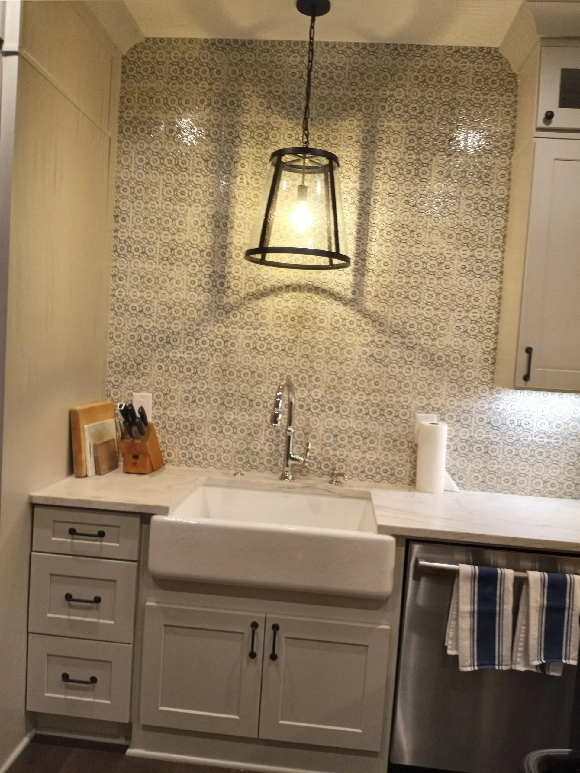 Kitchen sink with white cabinets, farmhouse sink, patterned backsplash, and pendant light.