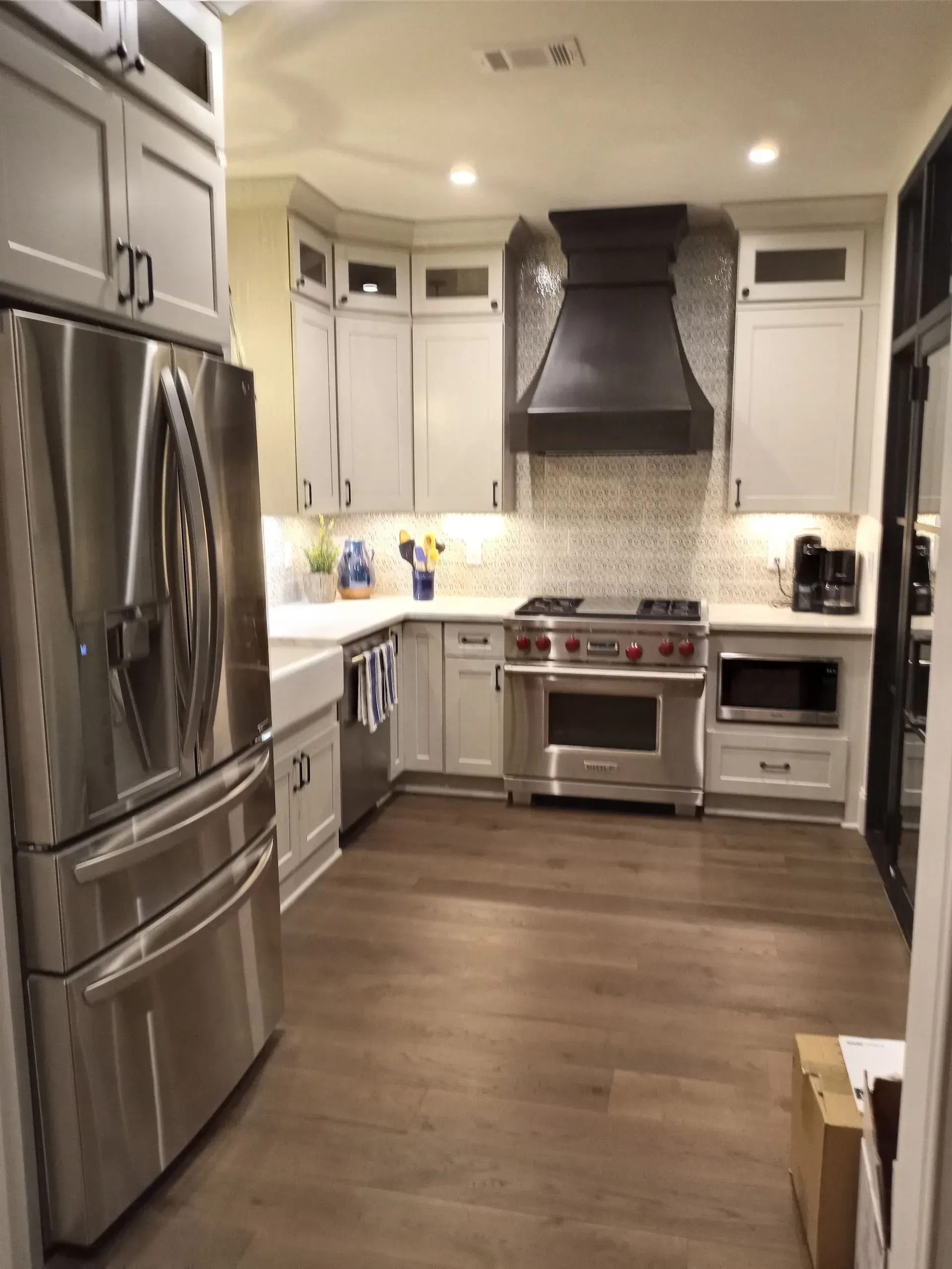 Modern kitchen with stainless steel appliances, light gray cabinets, and a dark range hood.