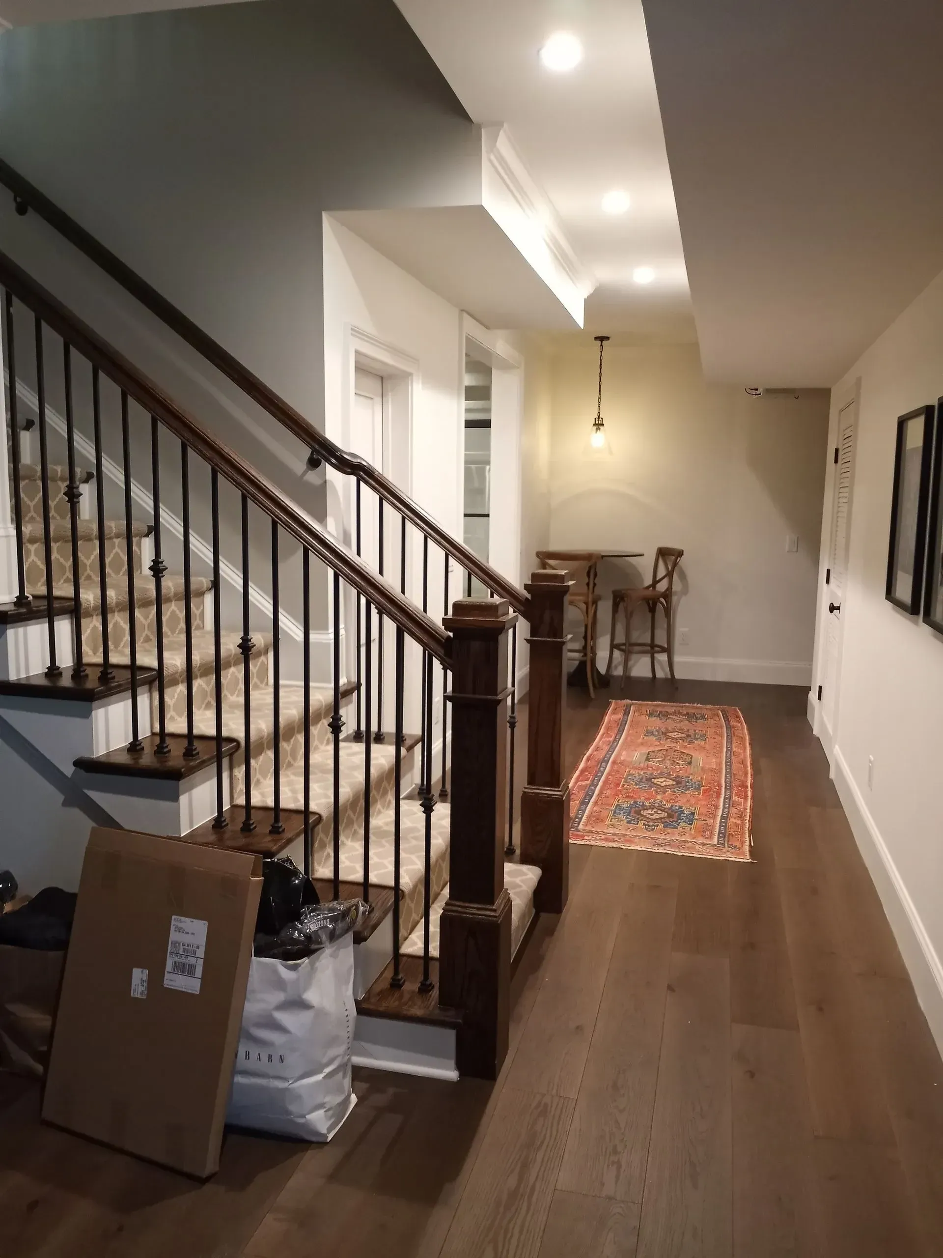 Staircase with dark wood banister and wrought iron railing, leading to a hallway with a rug and wooden floor.