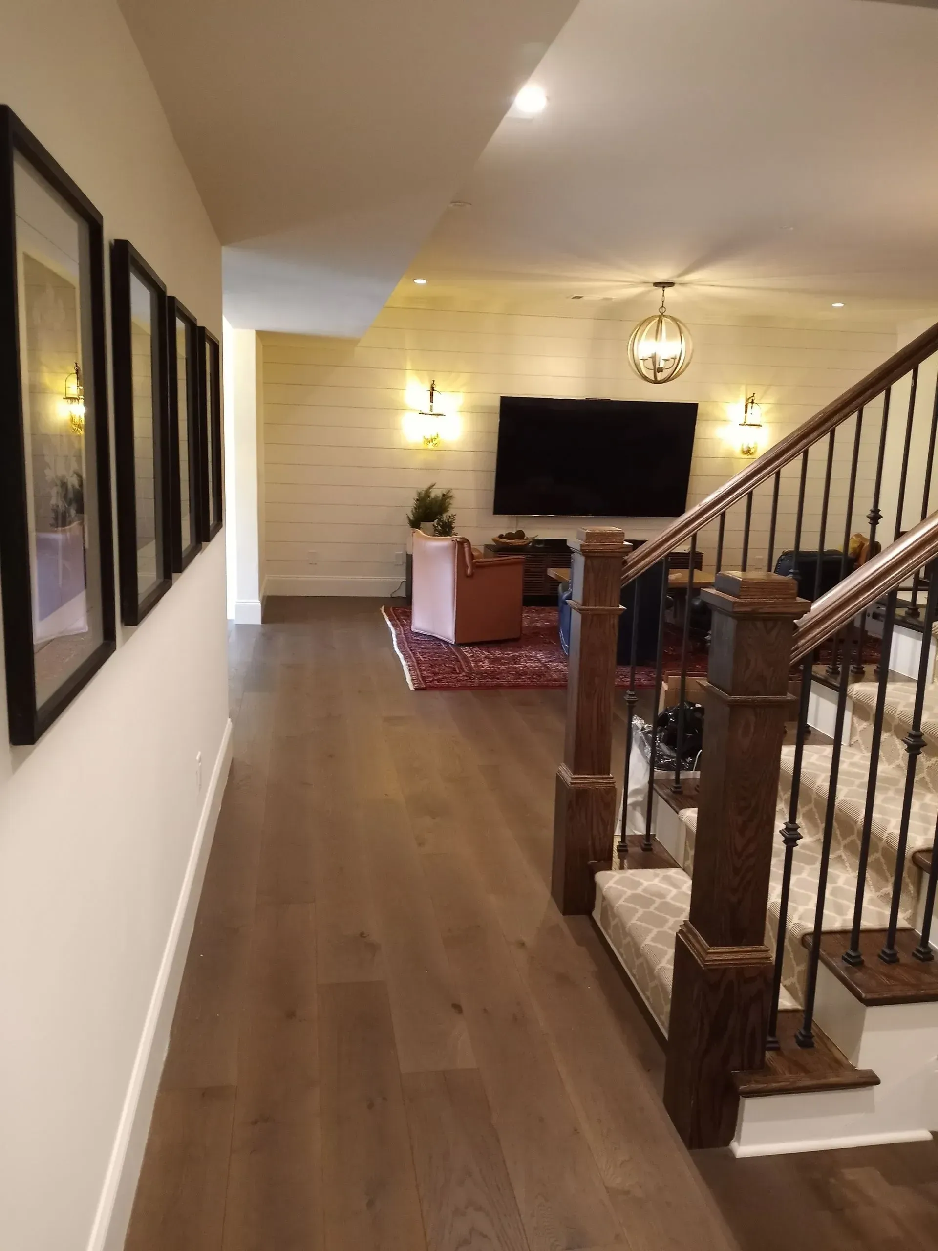 Hallway with hardwood floor, framed art, and staircase leading to a living area with TV and shiplap wall.