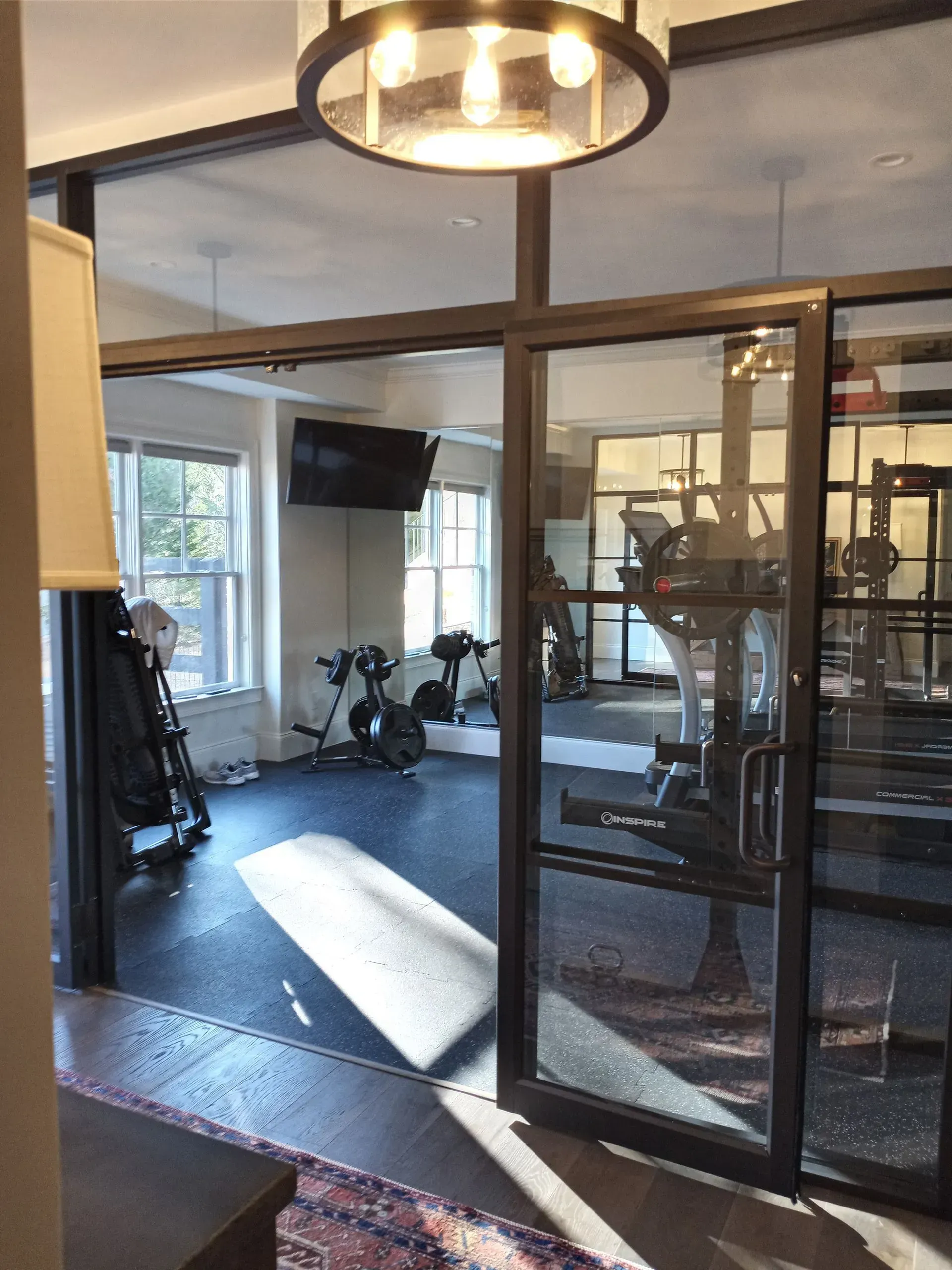 Glass-walled gym with exercise equipment visible; a sliding glass door is partially open, with overhead lighting.