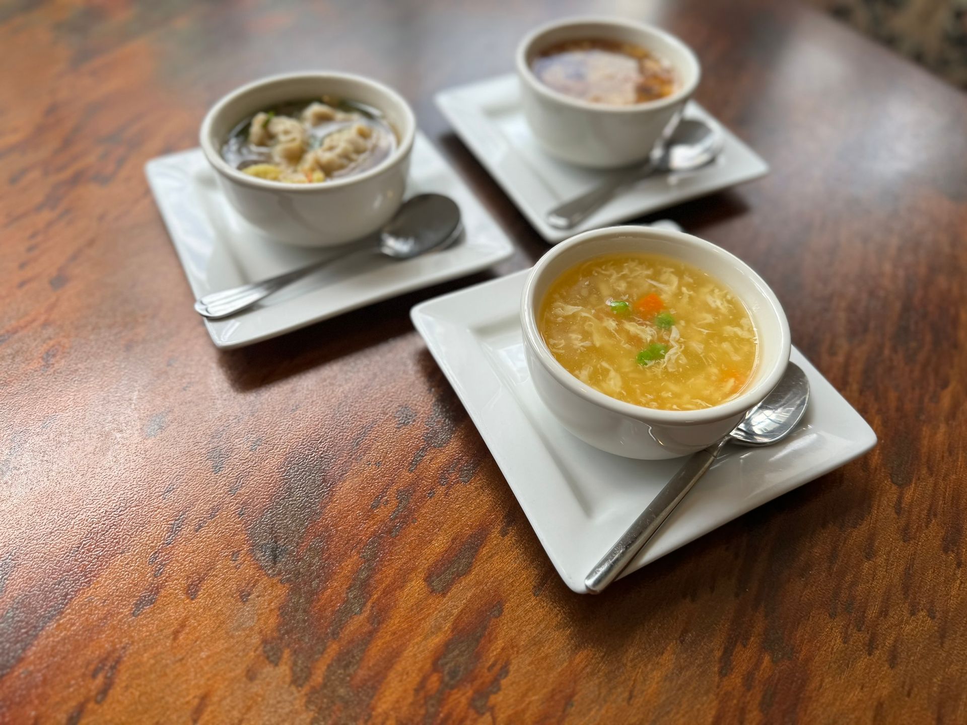 Three bowls of soup are sitting on a wooden table.
