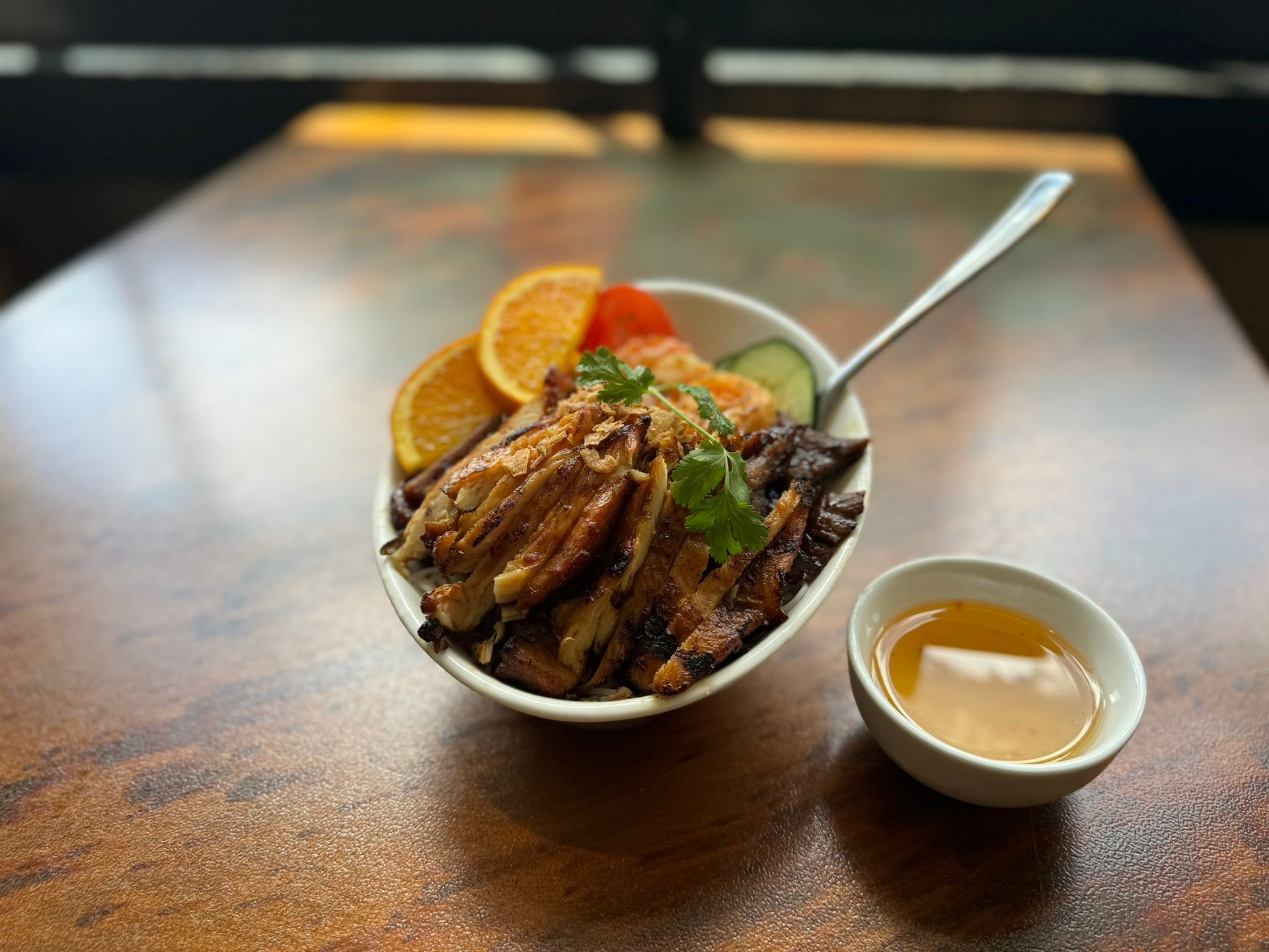 A bowl of food with a spoon in it is on a table next to a small bowl of sauce.
