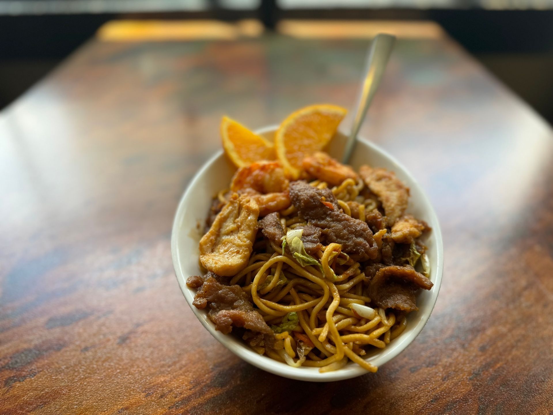 A bowl of noodles with meat and shrimp on a wooden table.