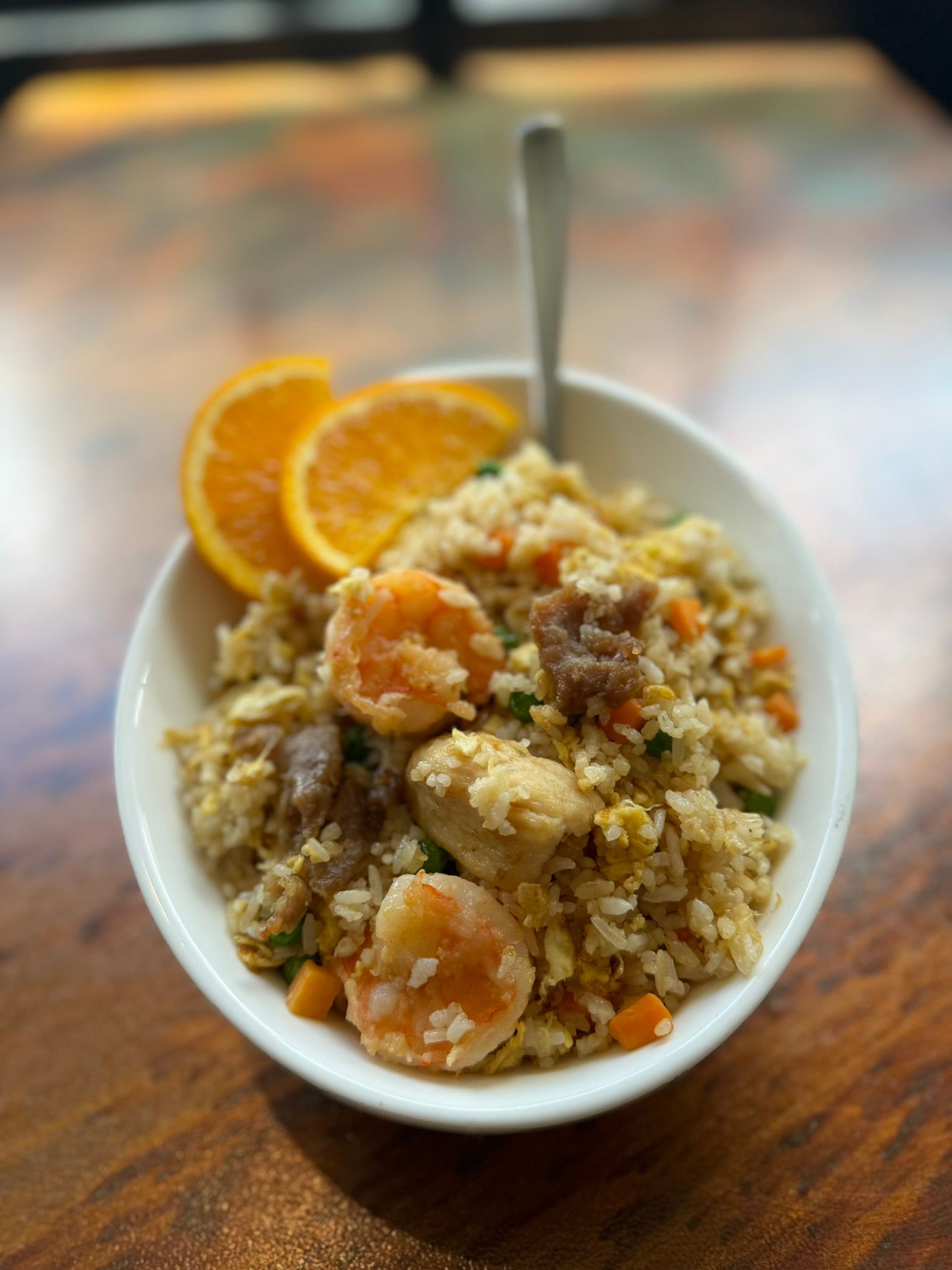 A bowl of fried rice with shrimp and chicken on a wooden table.