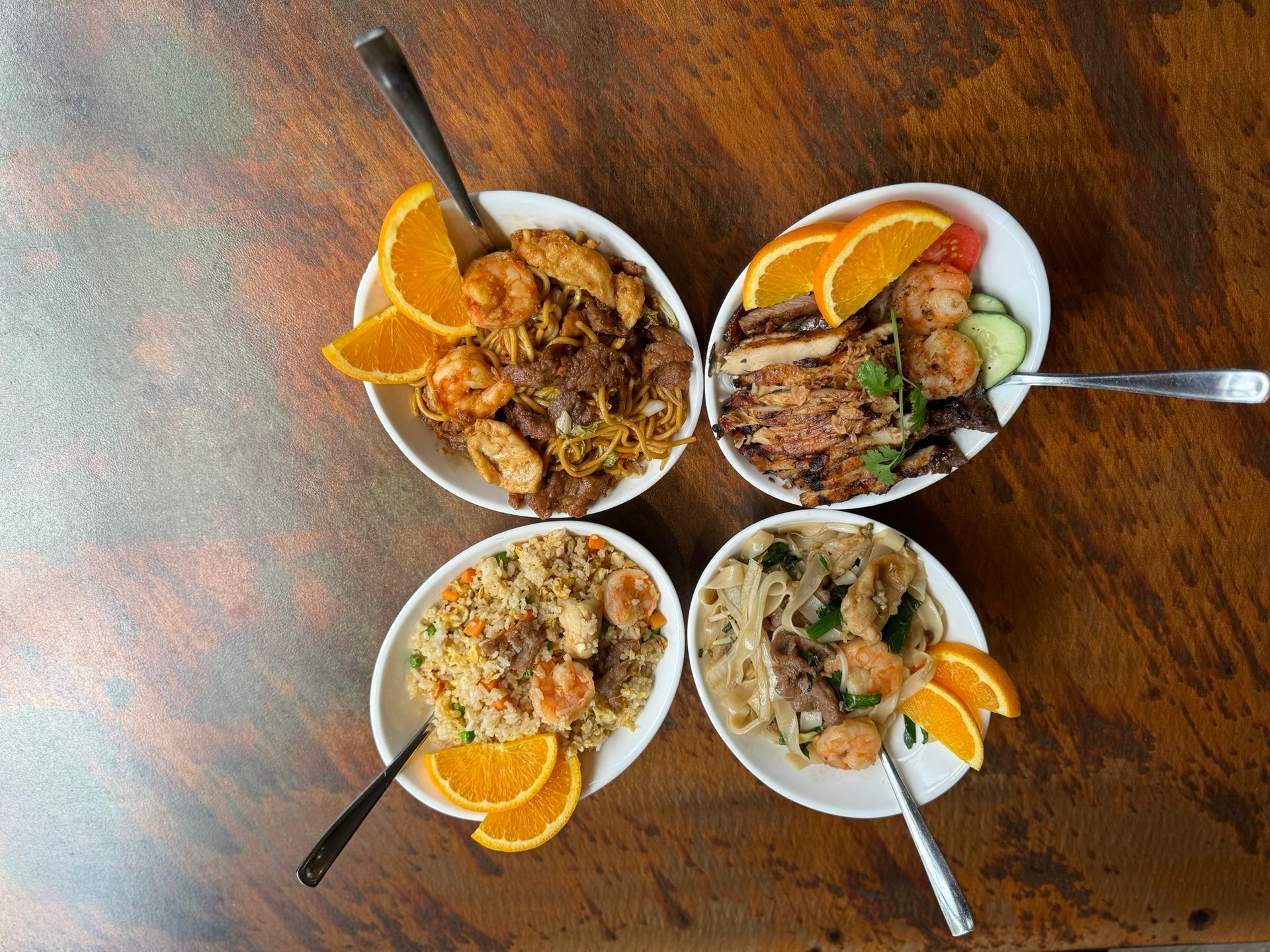 Four bowls of food with spoons on a wooden table.