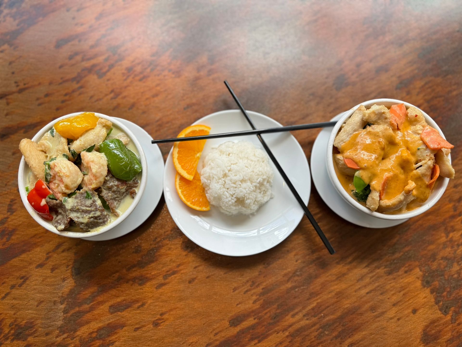 Three bowls of food with chopsticks on a wooden table.