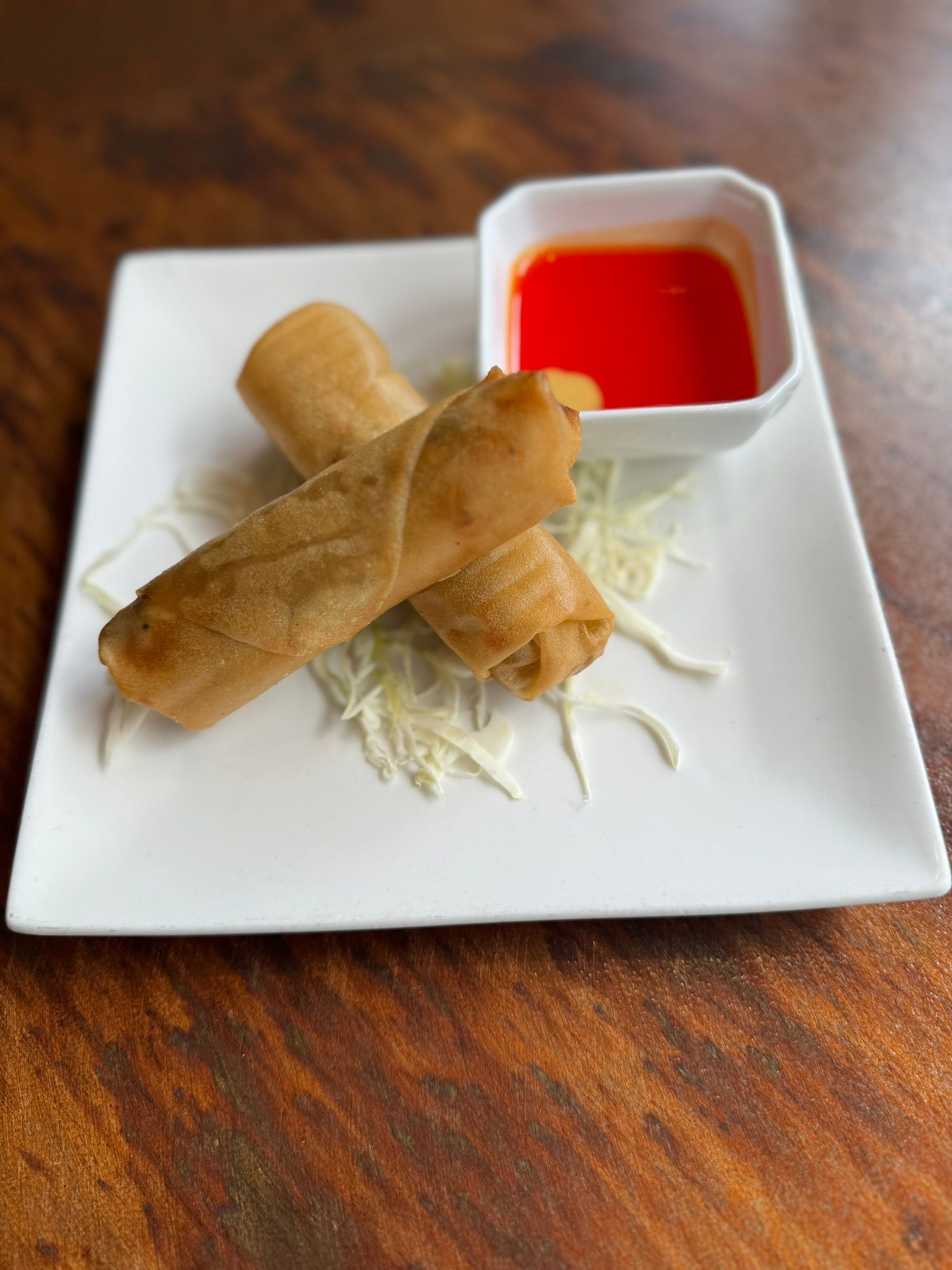 A white plate topped with two egg rolls and a small bowl of dipping sauce.