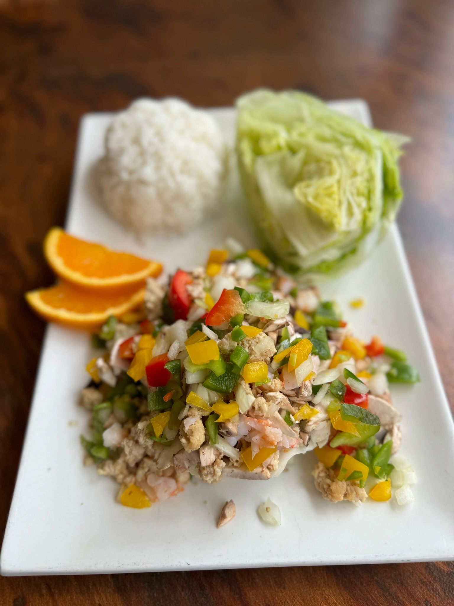 A white plate topped with a salad , lettuce , rice and oranges.
