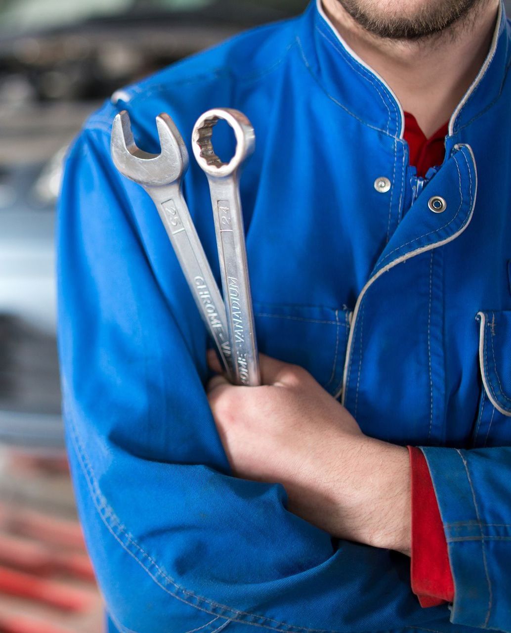 Mechanic holding wrenches, wearing a blue jumpsuit. | Matthews Automotive