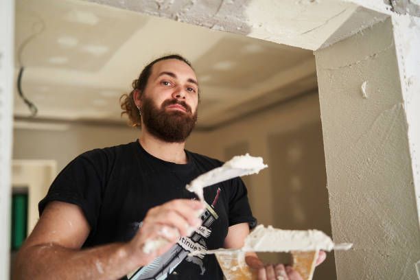 Man applying plaster to ceiling corner during residential plastering service project.