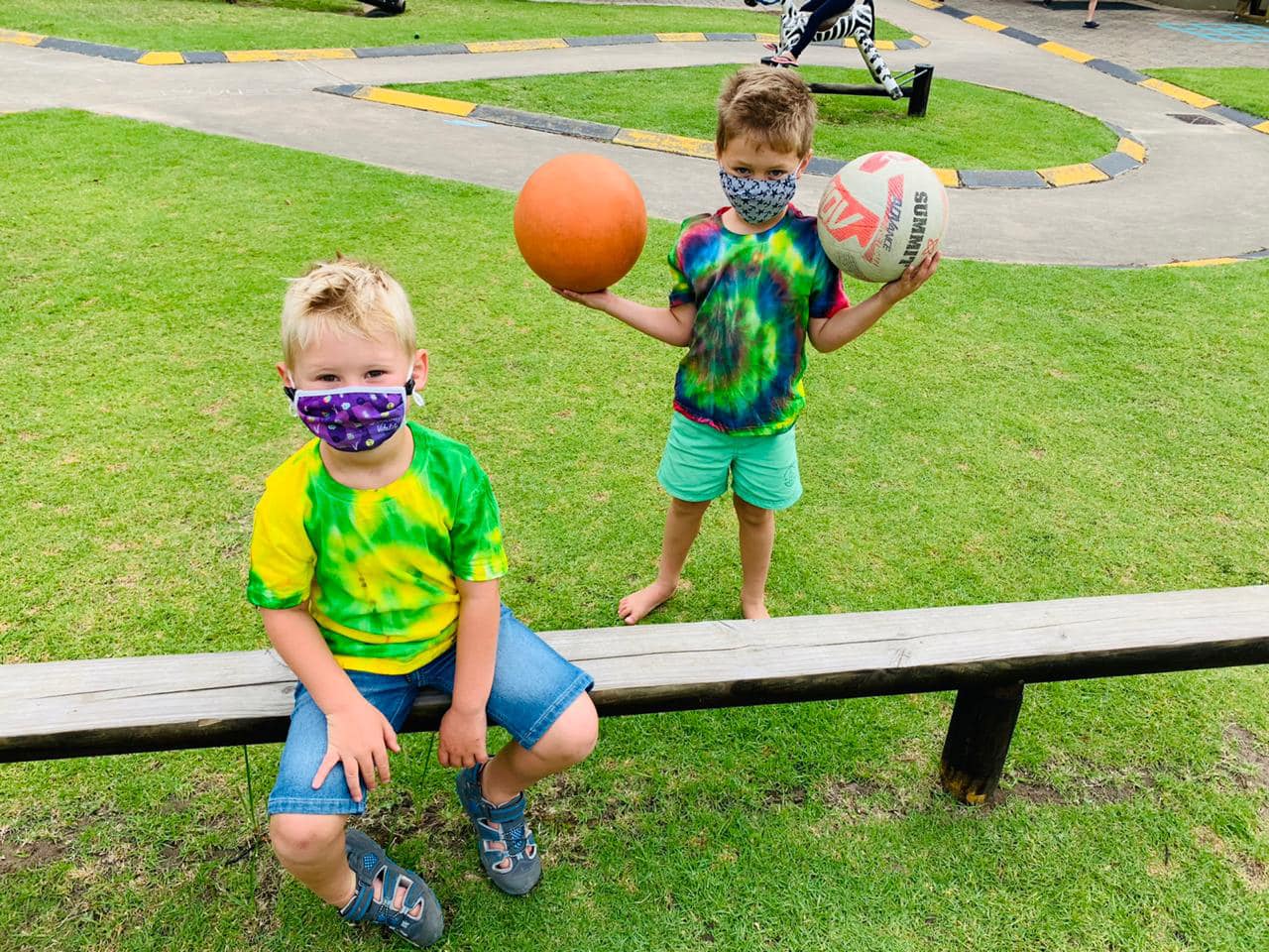 two children wearing face masks are sitting on a bench holding balls .