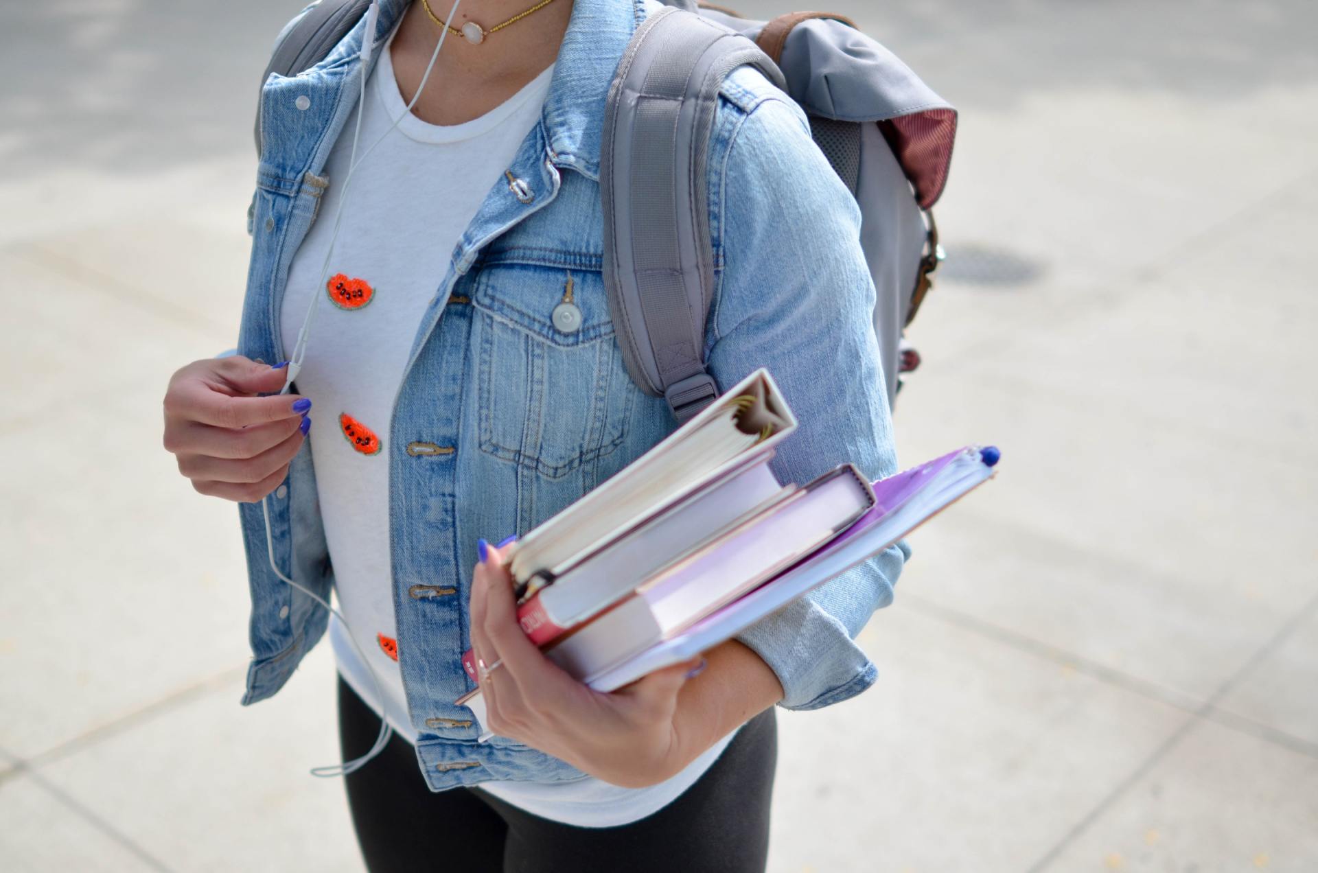 A woman with a backpack is holding a stack of books.