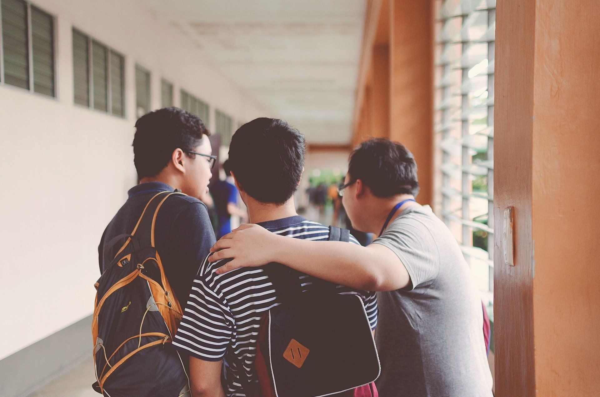 Three young men are hugging each other in a hallway.