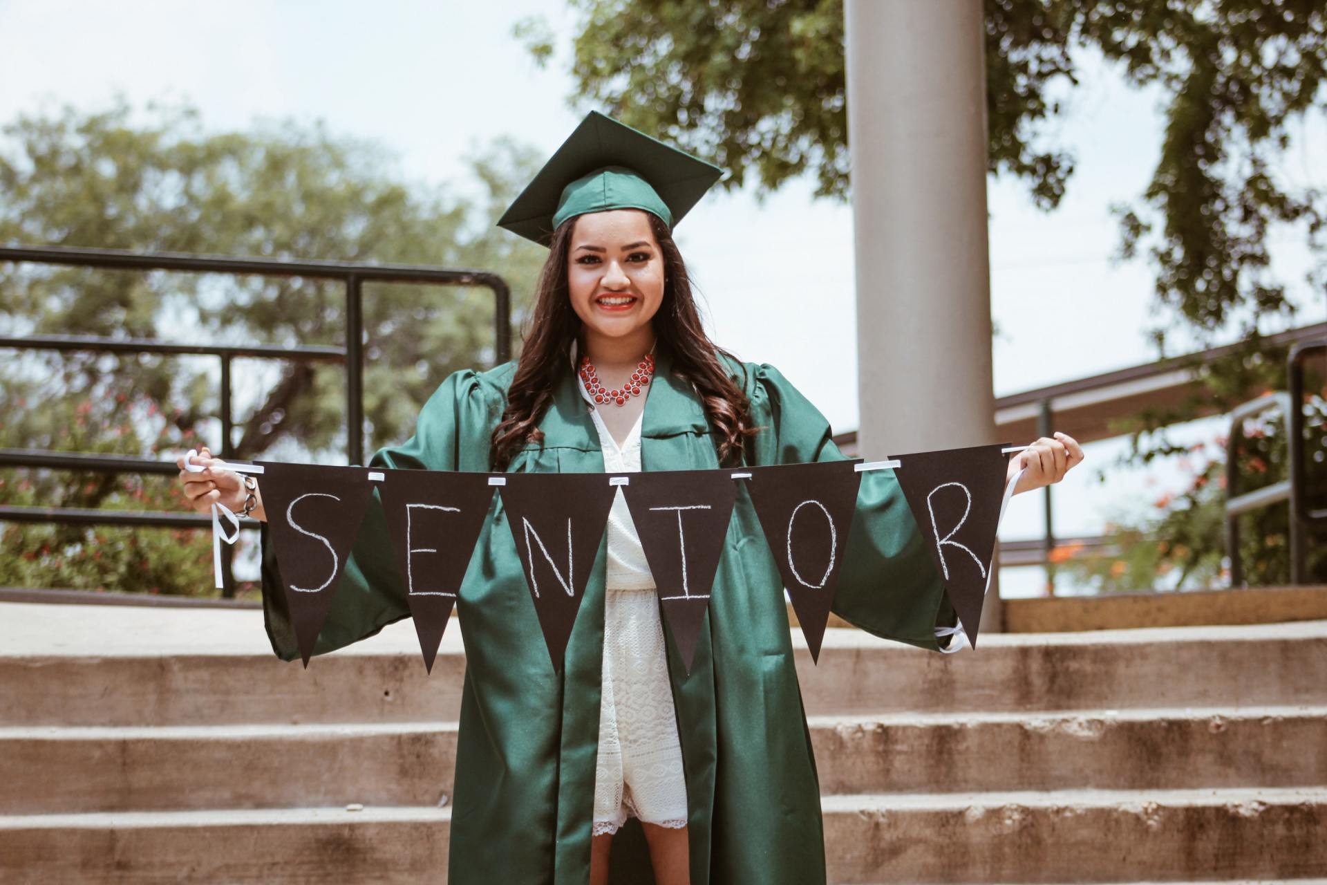 A woman in a graduation cap and gown is holding a banner that says senior.