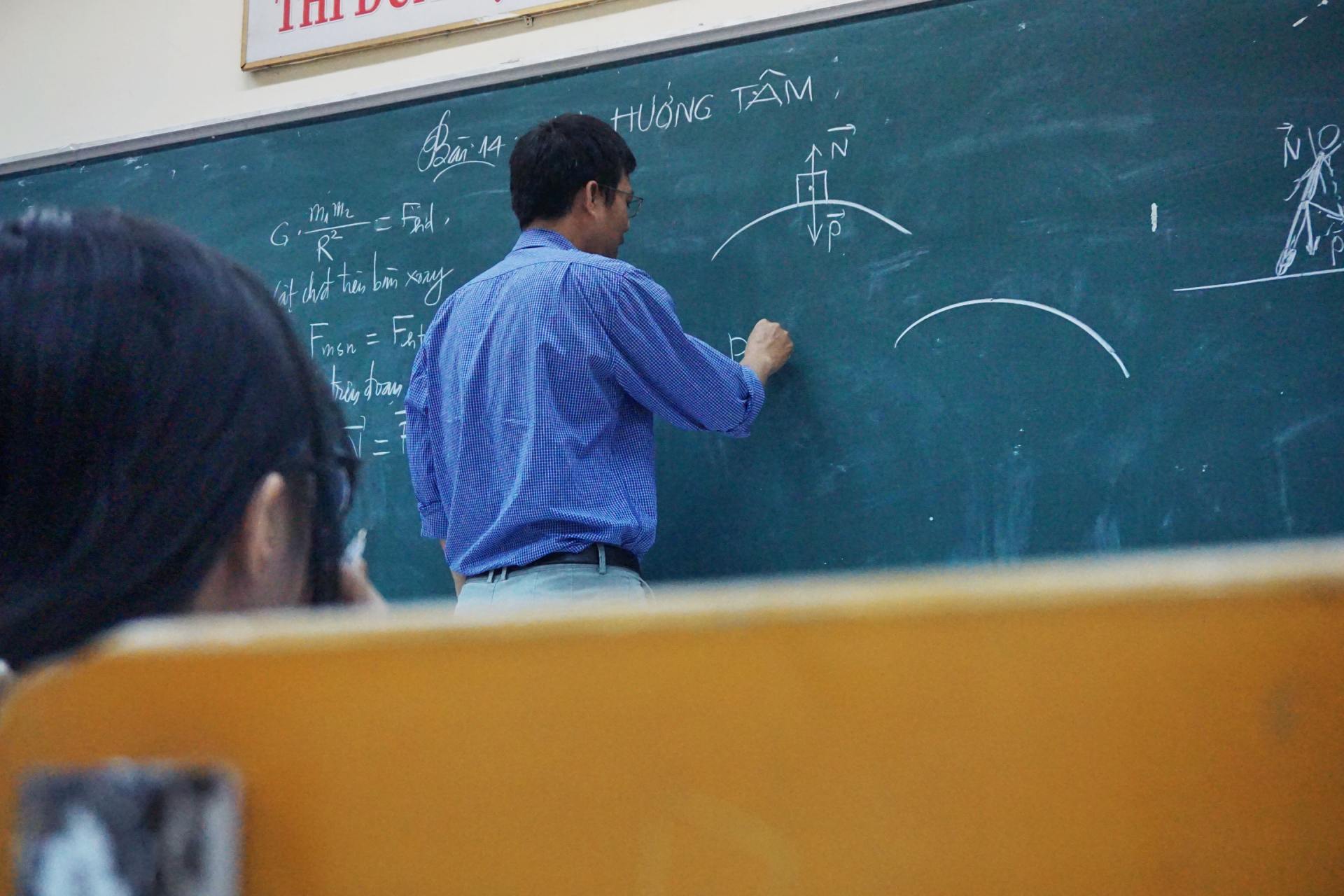 A man is writing on a blackboard in a classroom.