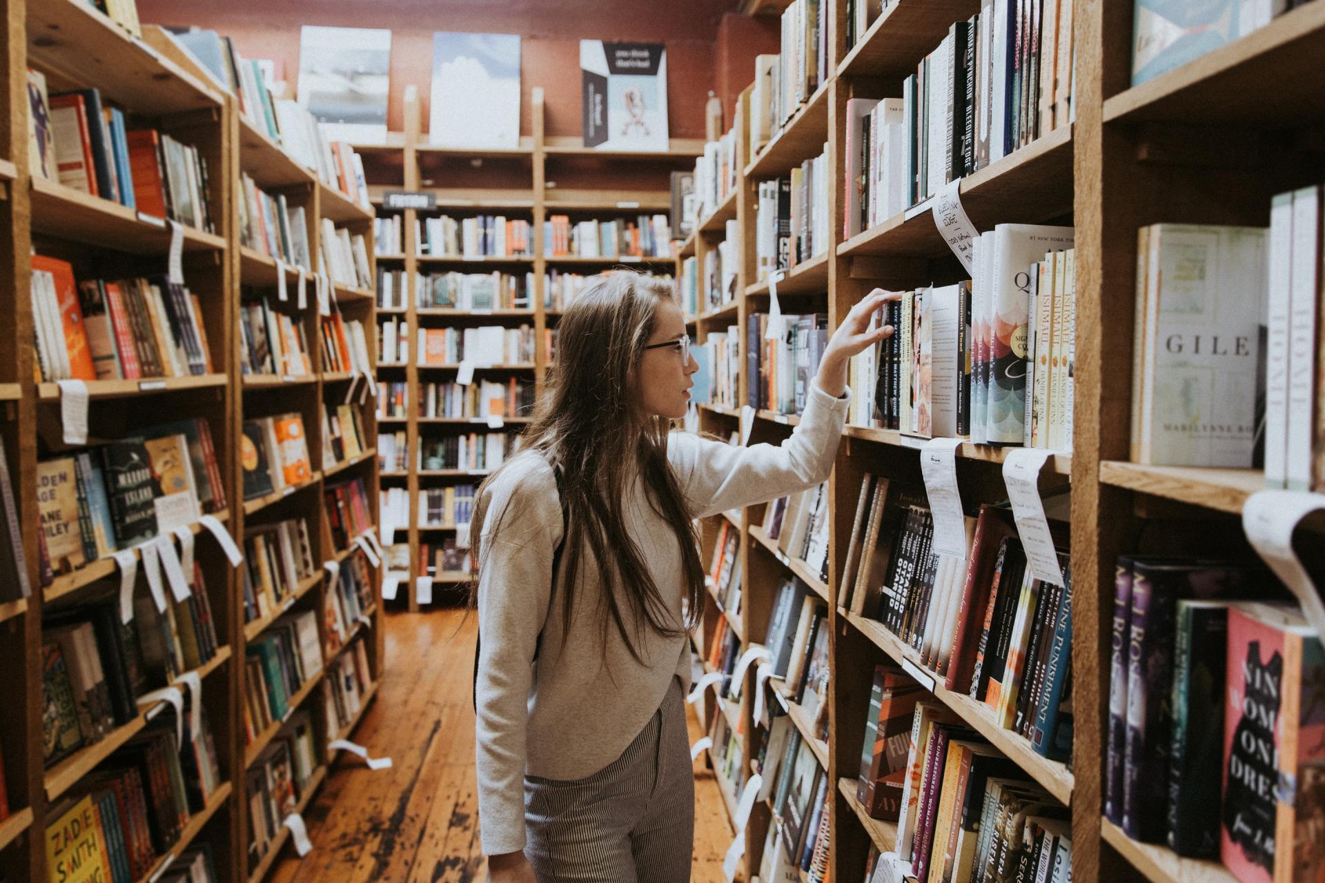 A woman is standing in a library looking at books on shelves.