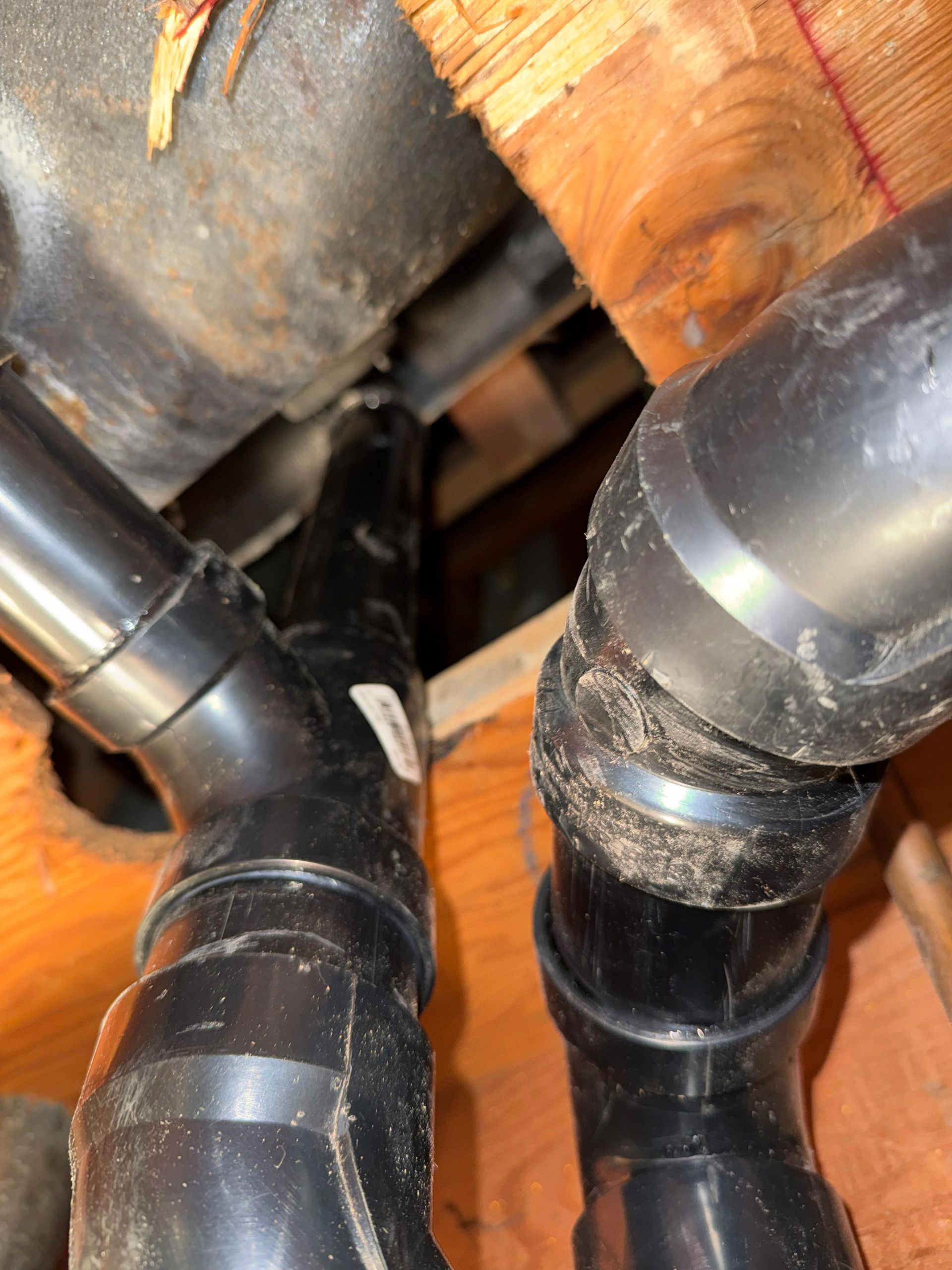 Black plumbing pipes connected to a gray drain pipe within a wooden structure.