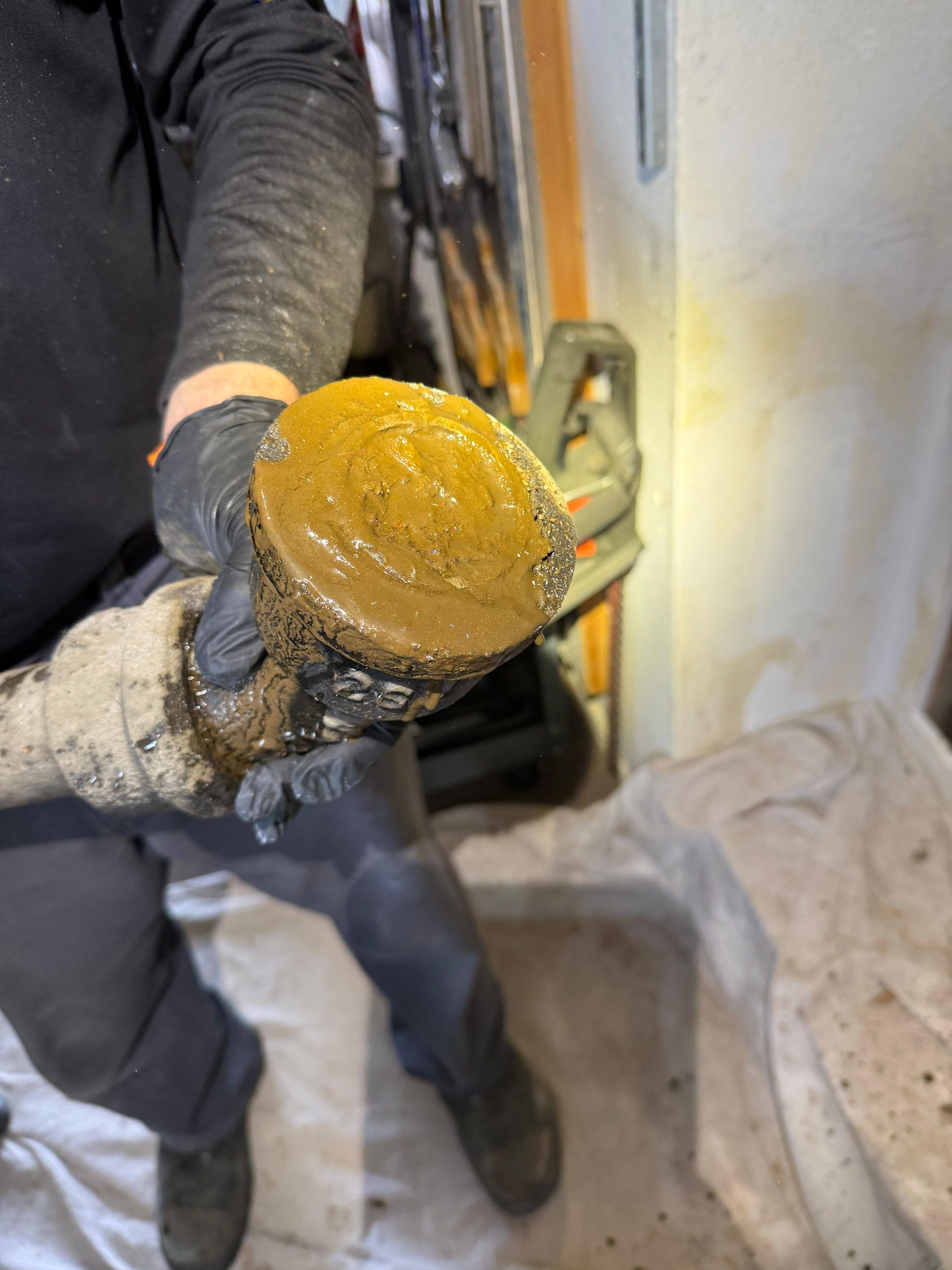 Person holding a large, dirty, circular object, possibly a filter. Gloves and dark clothing are visible.