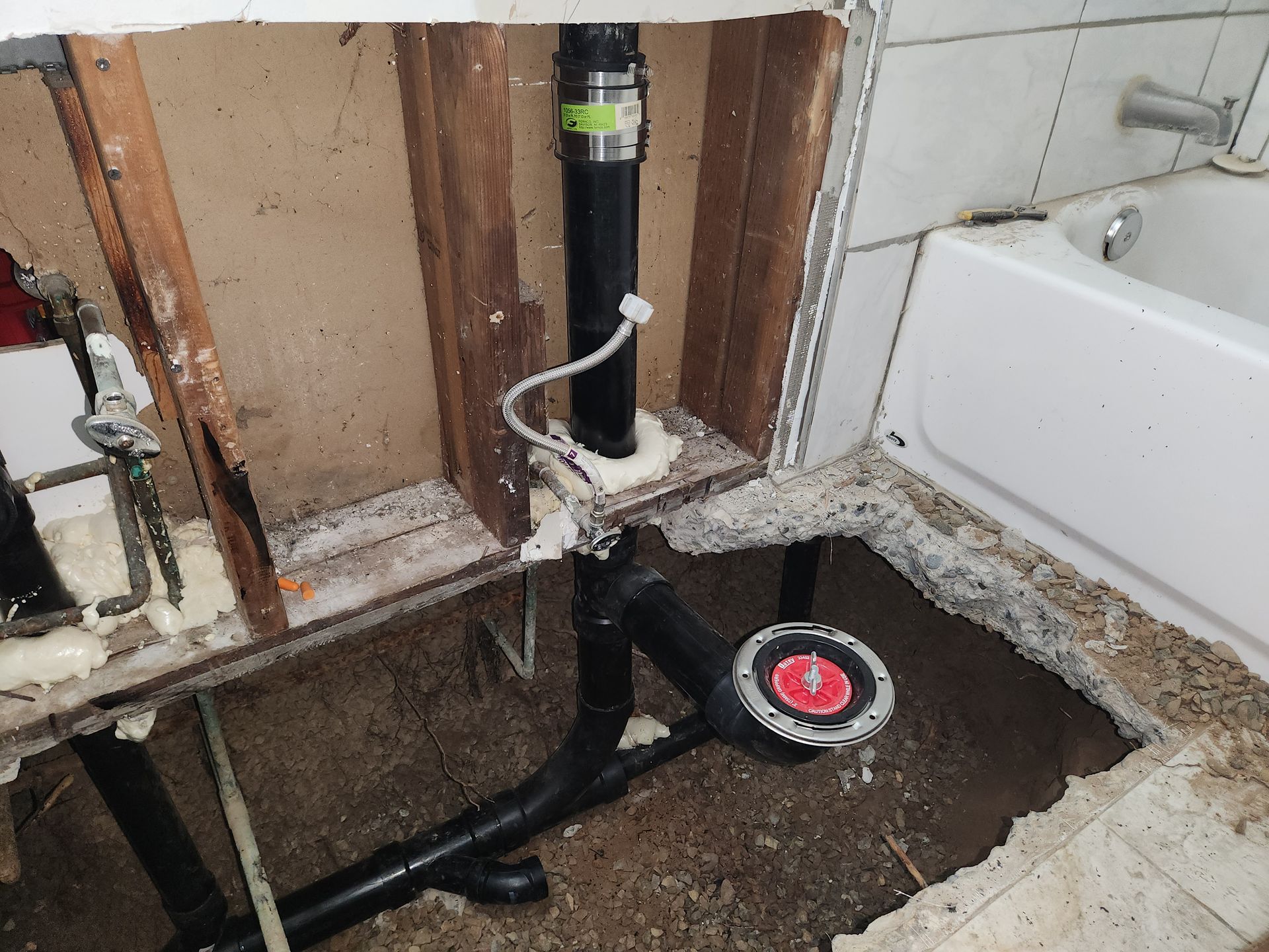 Bathroom plumbing exposed, showing black drain pipes, a red drain cap, and insulation foam.