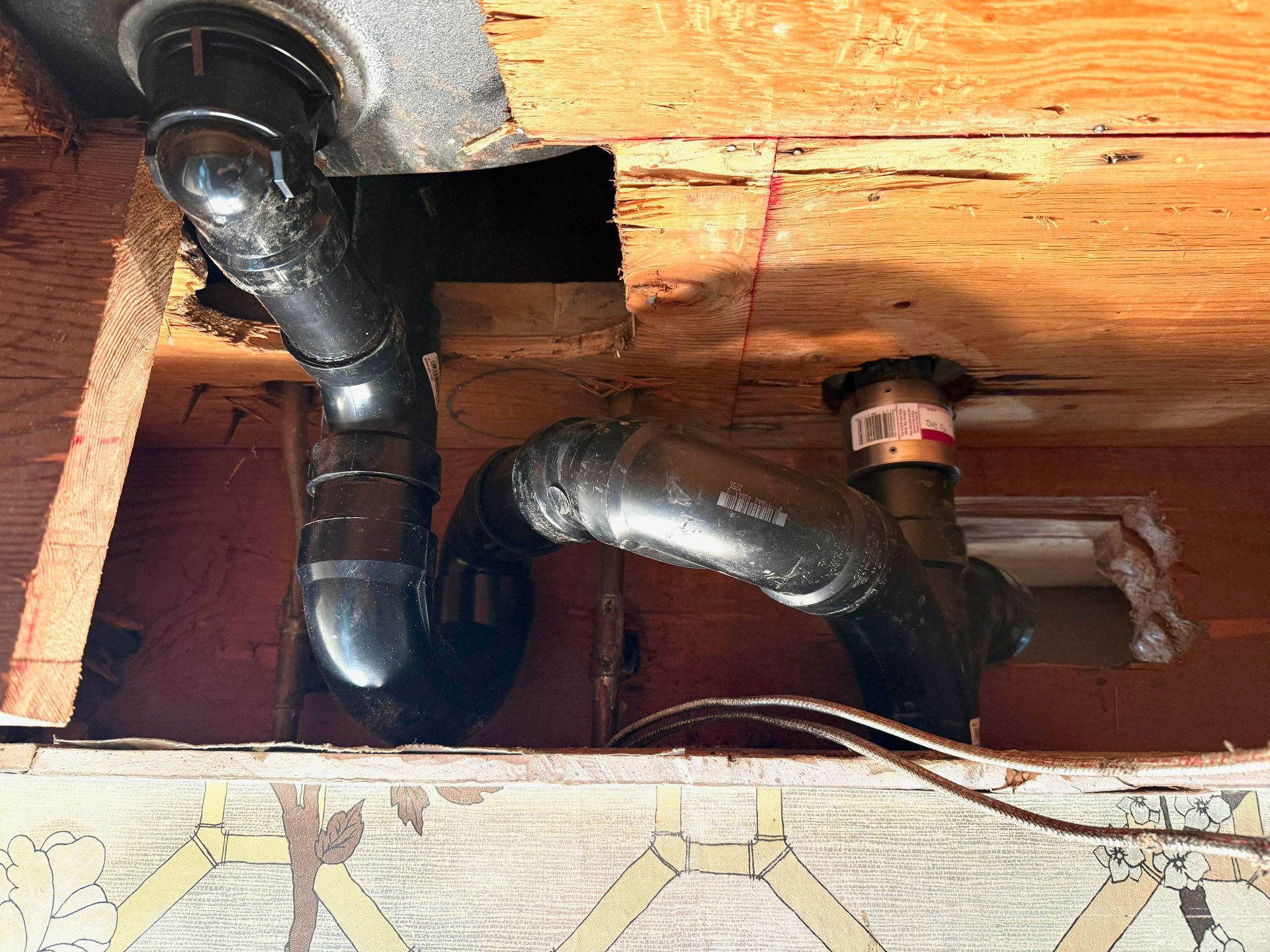 Black plumbing pipes under a wooden structure, forming a complex drain system.