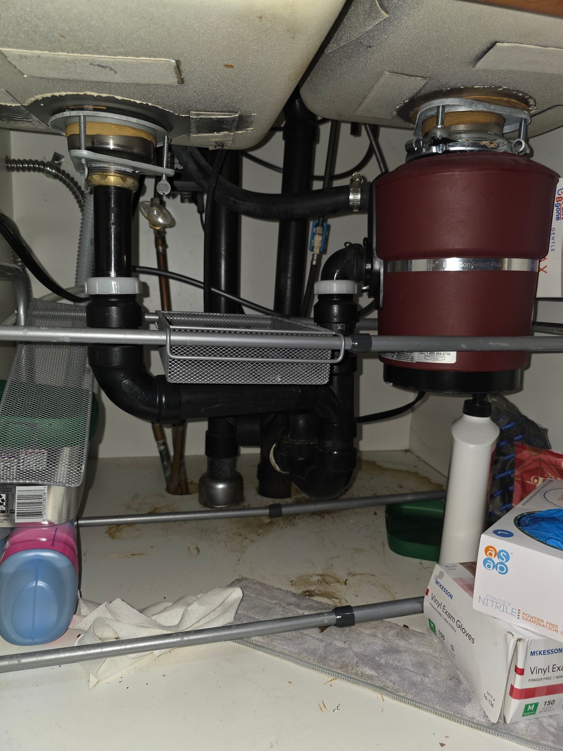 Under kitchen sink: plumbing with garbage disposal, black pipes, and sink basins.