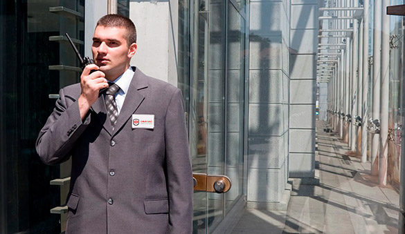 Un guardia de seguridad hablando por radio fuera de un edificio de cristal.