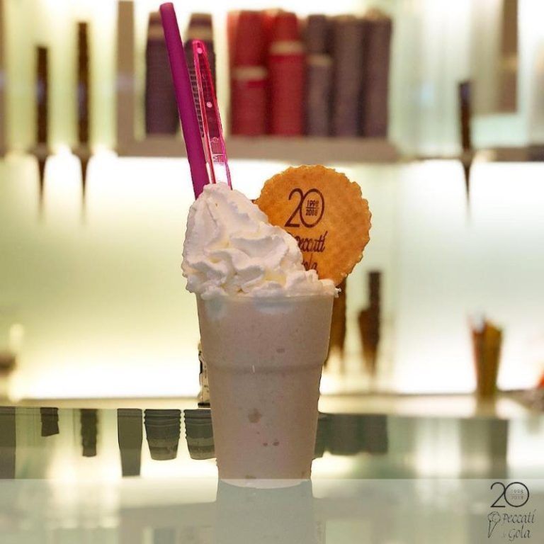 Milkshake rosa guarnito con panna montata e un biscotto, con cannucce rosa su un bancone riflettente.