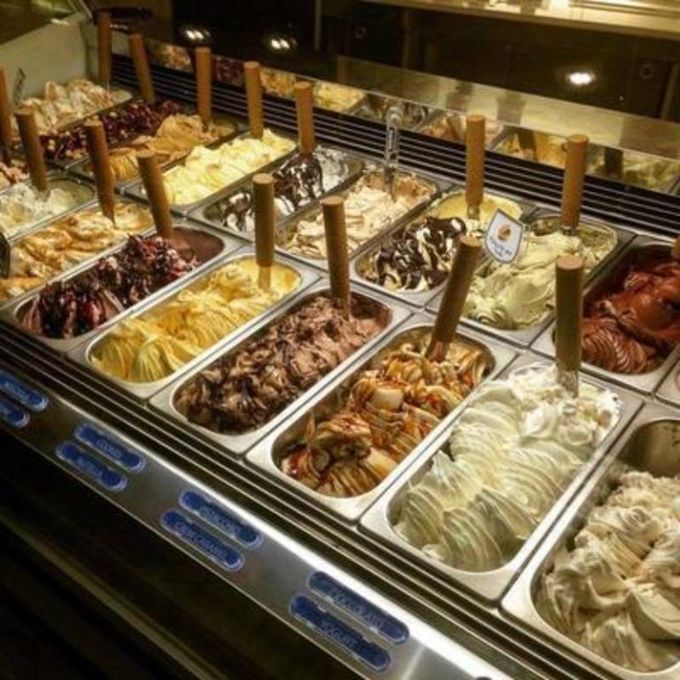 Assortimento di gusti di gelato in vaschette di metallo con palette per servirlo al bancone del gelato.