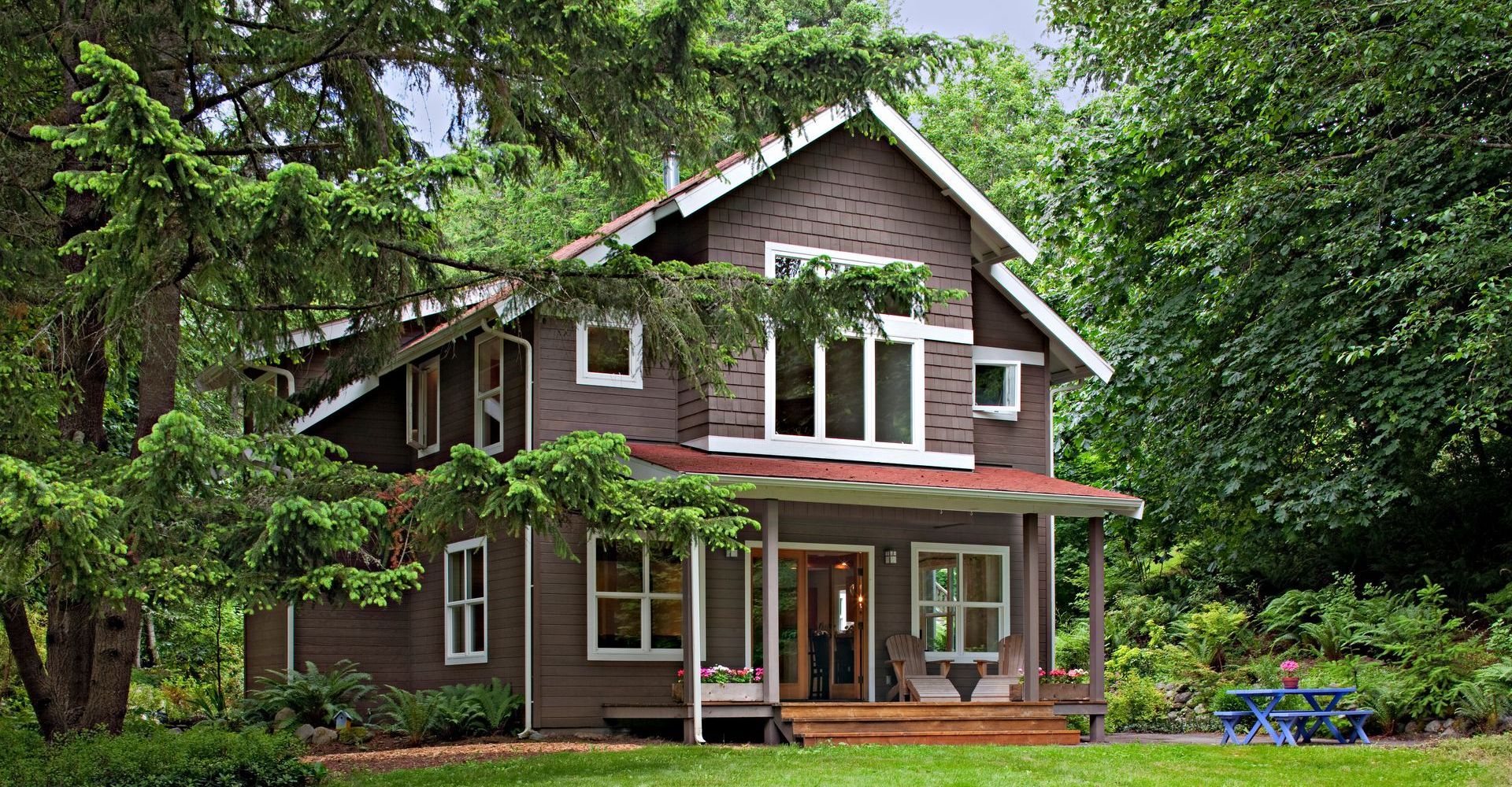 A large brown house with a red roof is surrounded by trees and grass.
