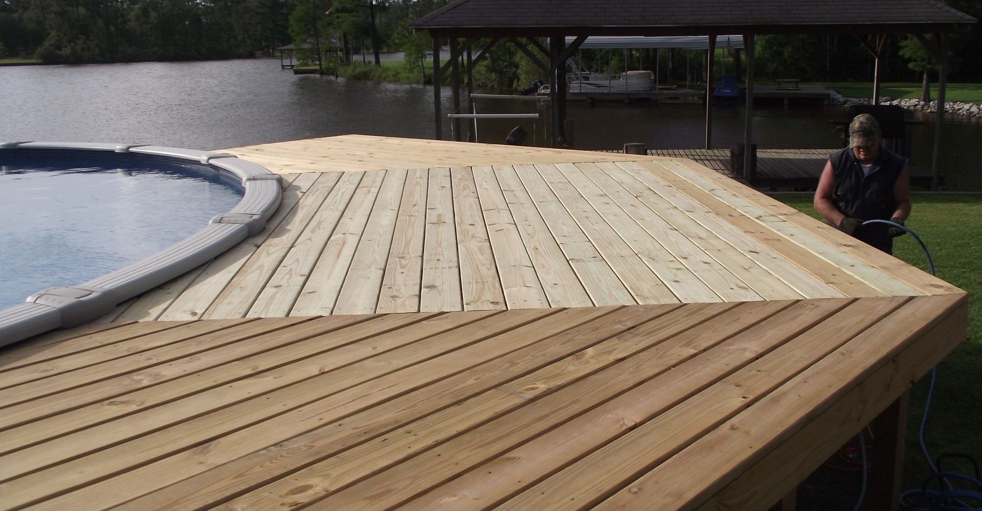 A man is working on a wooden deck next to a pool.