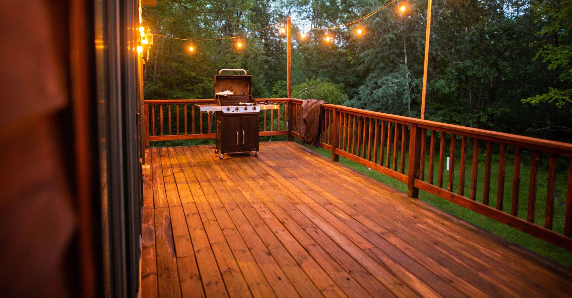 A wooden deck with a grill and string lights on it.