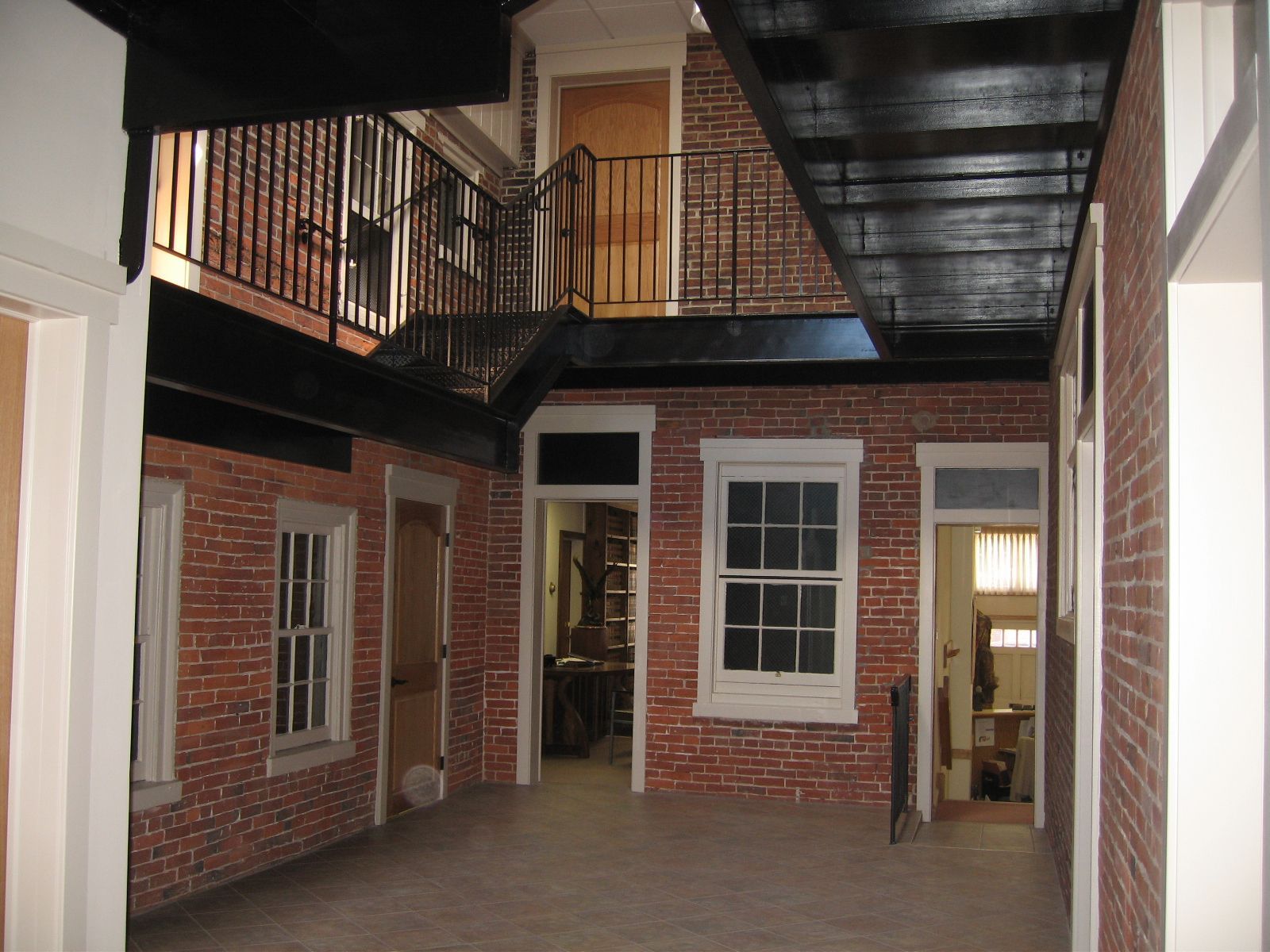 Brick interior with balcony, doorway, and windows. Black metal railing, white trim, and gray floor.