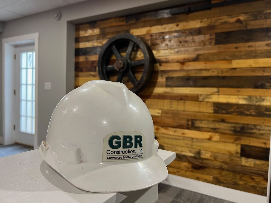 A white hard hat is sitting on a counter in front of a wooden wall.