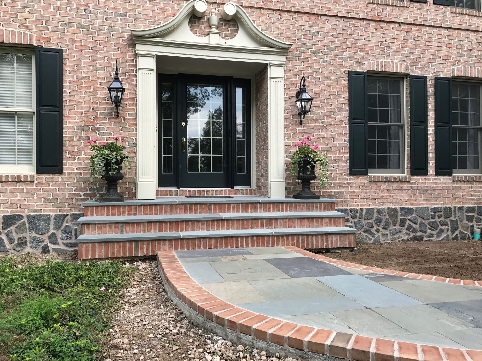 A brick house with black shutters and a brick walkway leading to the front door.