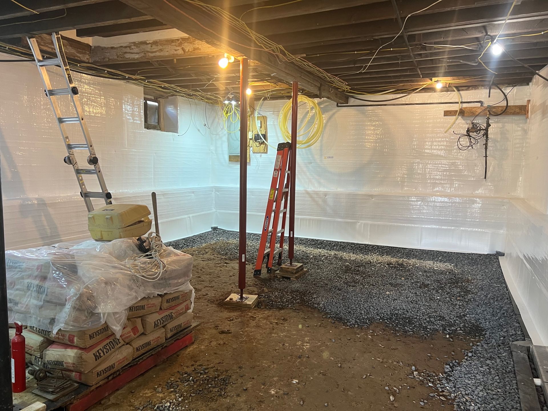 A basement with a ladder and bags of gravel in it.