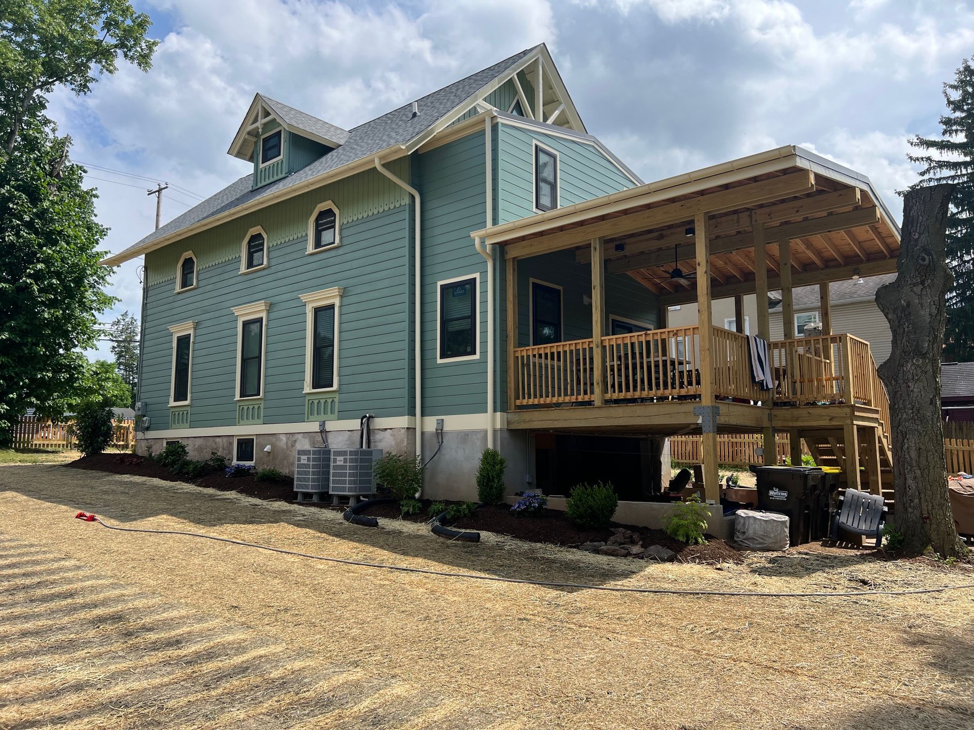 A large green house with a wooden deck and porch.