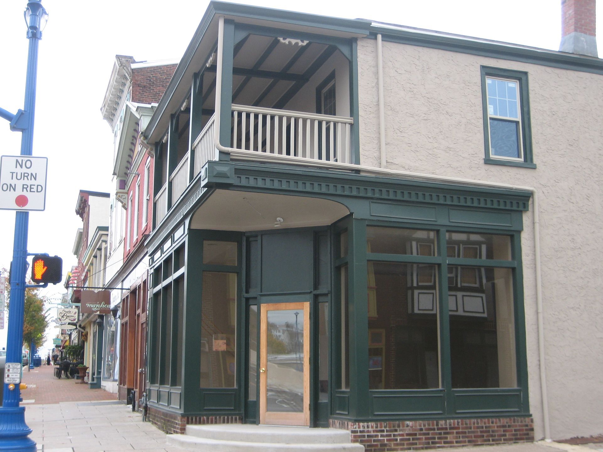 Building with storefront and second-story balcony; green trim, cream walls, sidewalk, street sign, and blue lamp post.
