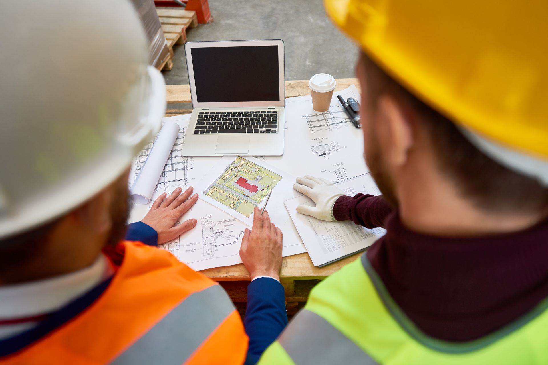 Two construction workers are sitting at a table looking at a laptop.